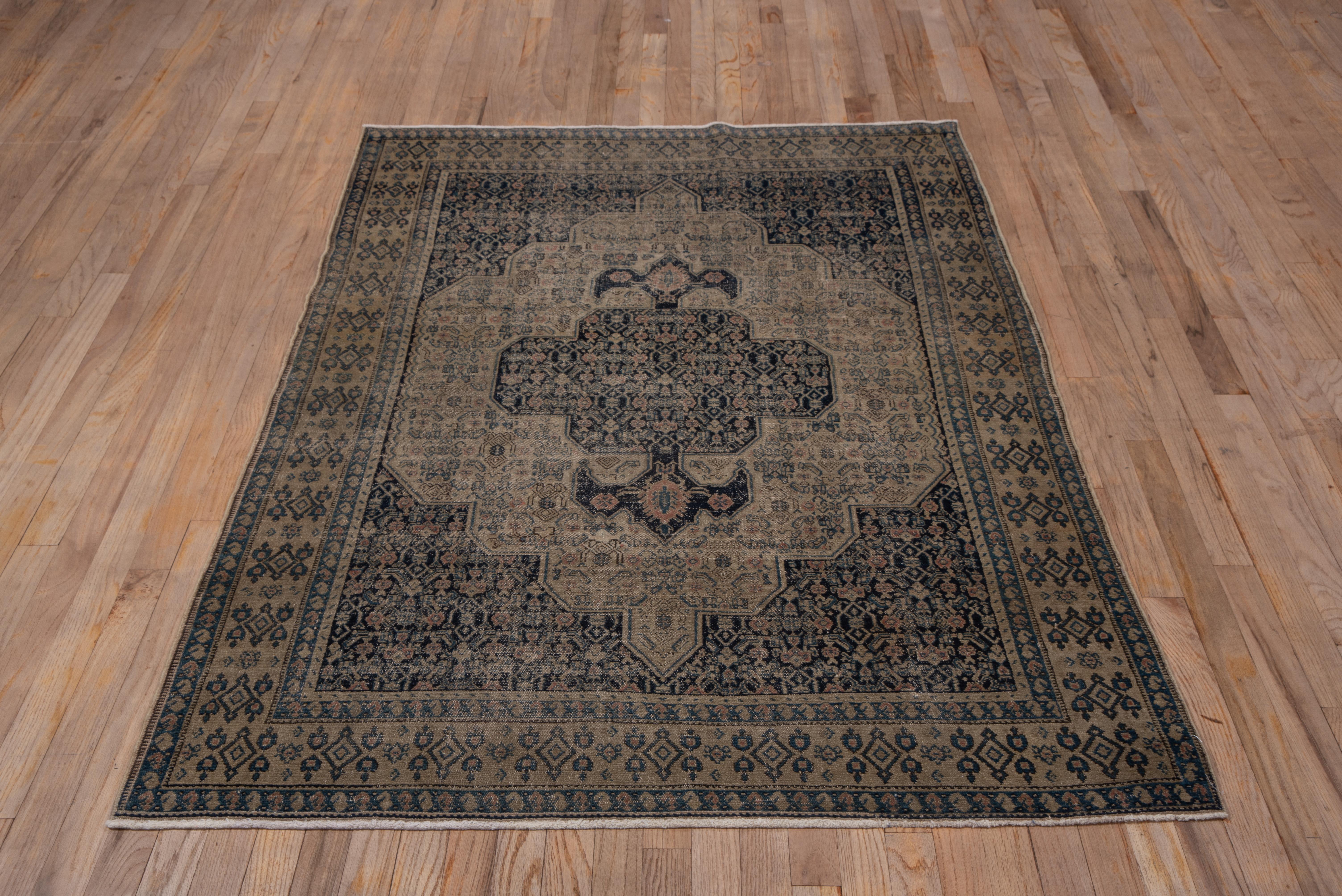 This finely knotted, but rather distressed Kurdish urban scatter shows a dark blue ground and anchor pendanted quadrifoil medallion with a small Herati design which continues in the same scale into the beige, pointed and lobed Sub field. The straw