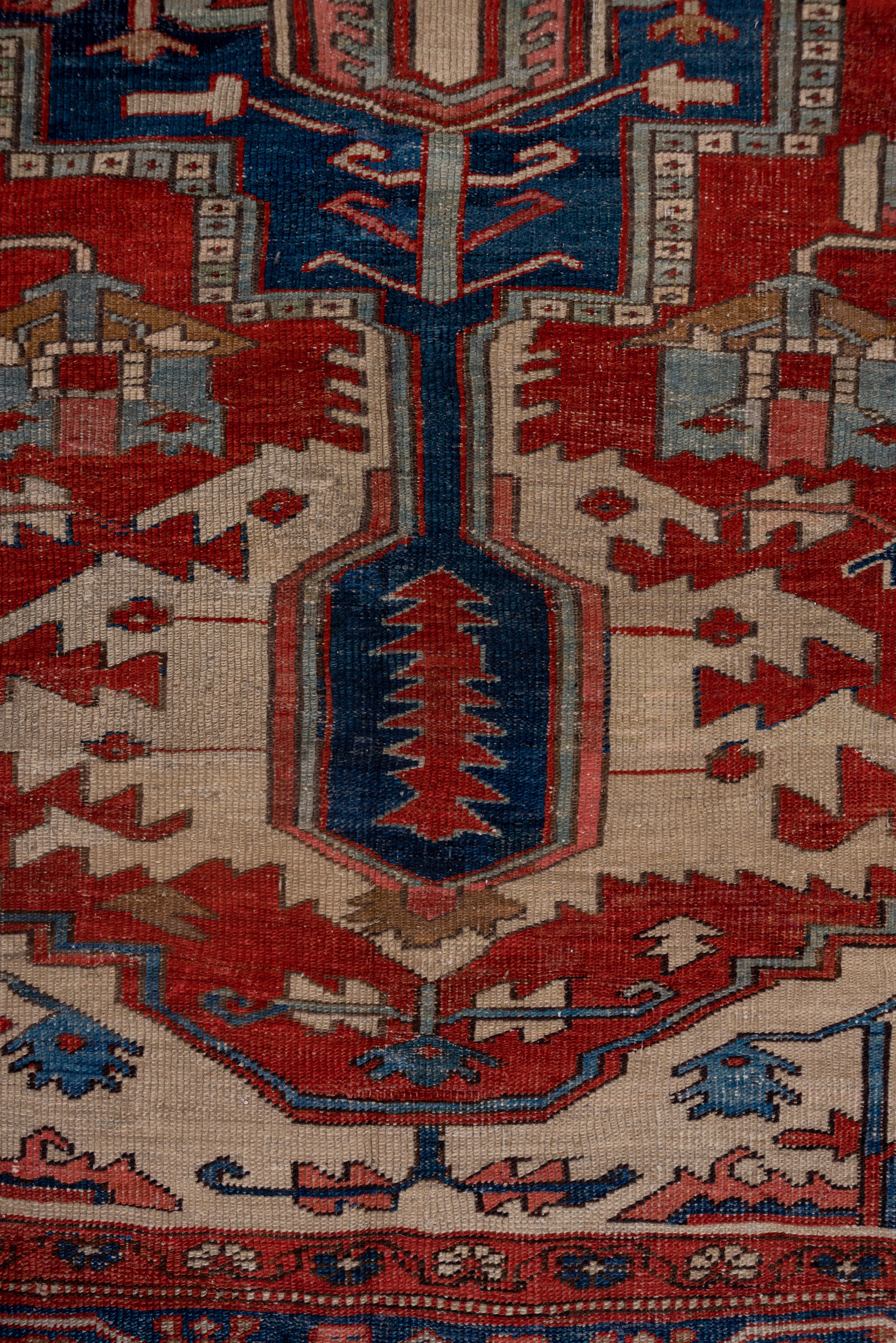 Classic Serapi quality NW Persian carpet with a natural dye palette and cotton foundation. The madder field shows a sometimes connected scatter of geometric leaves and flowers, centralized by a stepped blue medallion with dramatic sand ragged