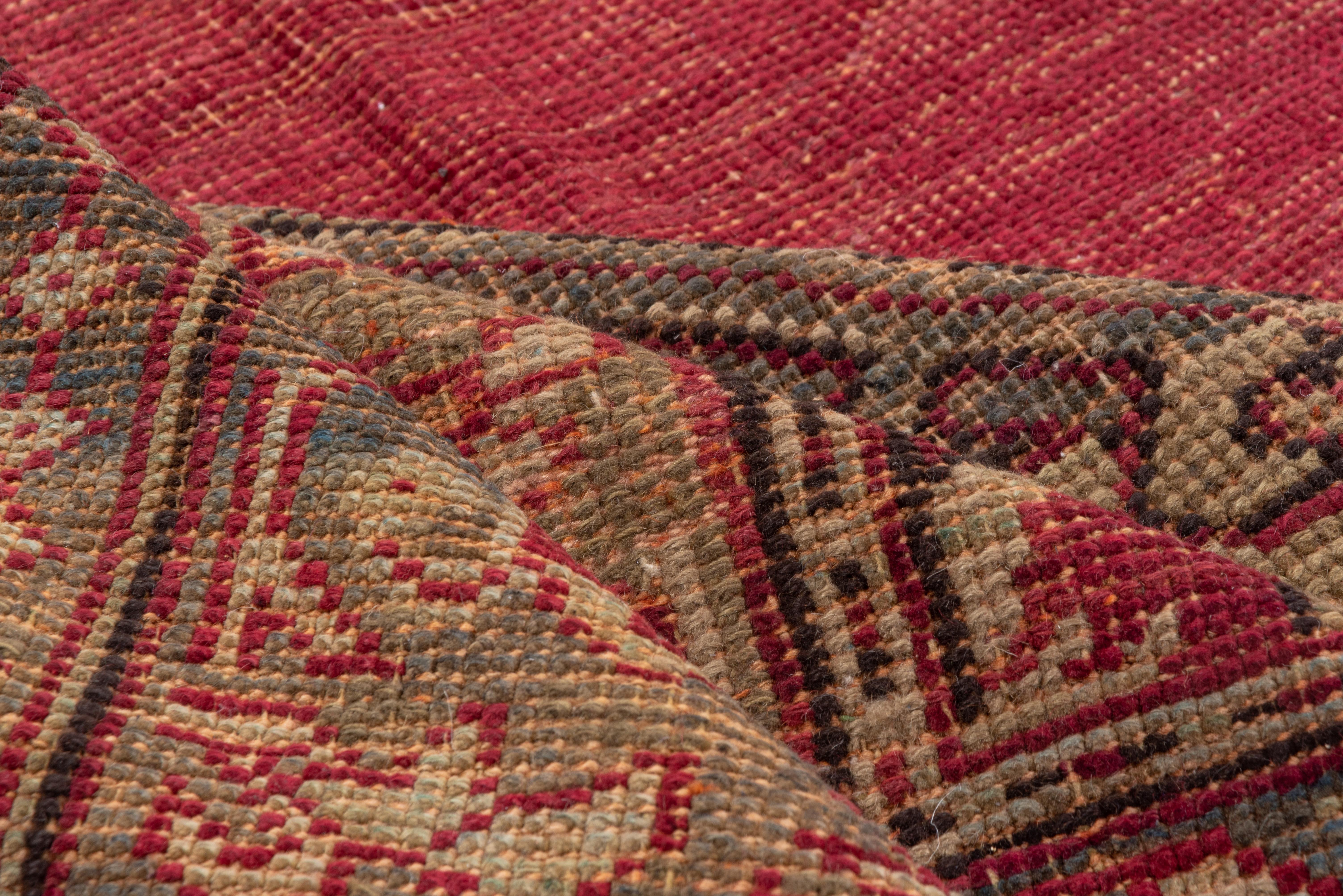 This Oushak carpet is very bold and direct, with an abrashed garnet red field centered by a giant pointed cross medallion positioned by huge, hooked volutes devolving from the nearly triangular corners. Abrashed green accents. Tilted palmette
