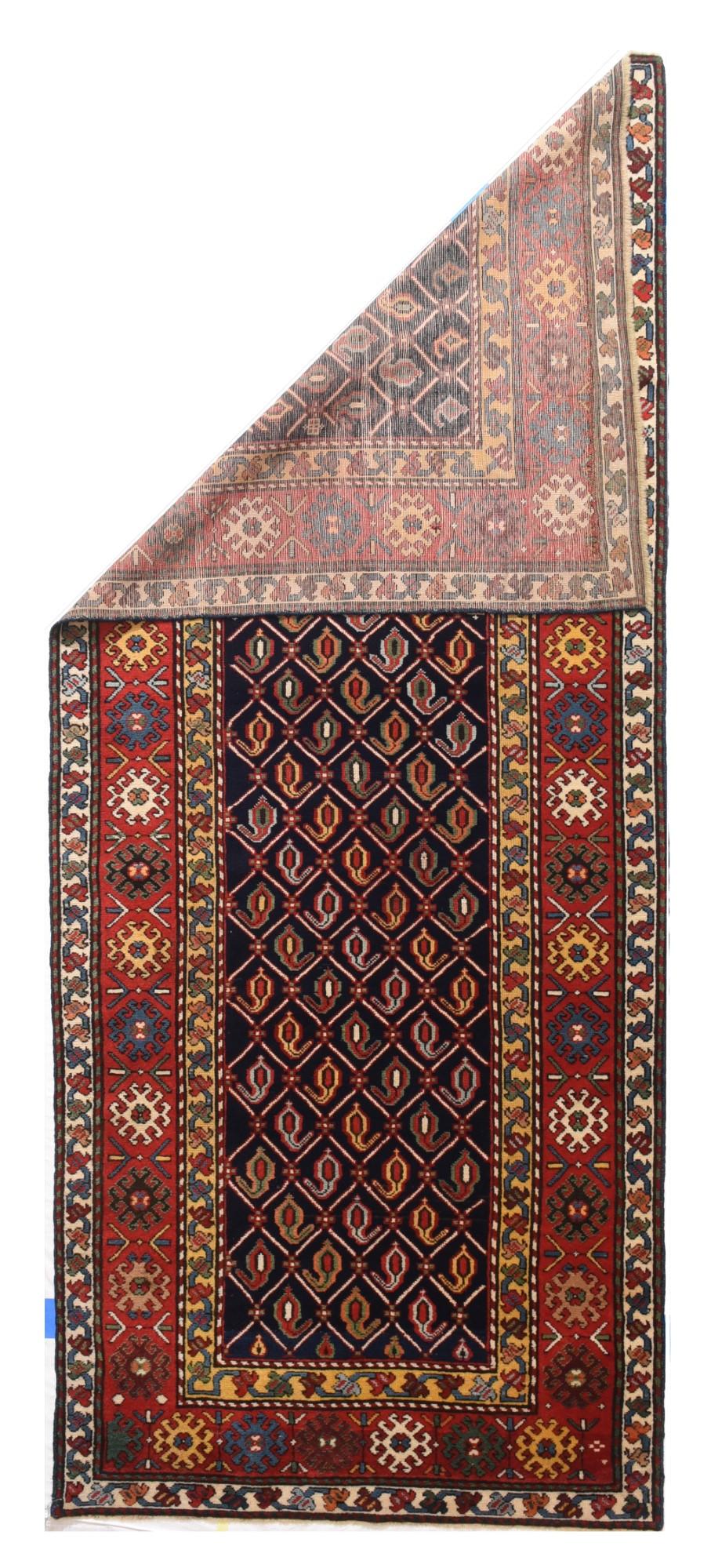 From the southern Caucasus, this good condition long piece presents a dark indigo blue field decorated with a diamond lattice enclosing row by row reversing botehs, but all in one general direction. Madder red main border with ivory, yellow, near