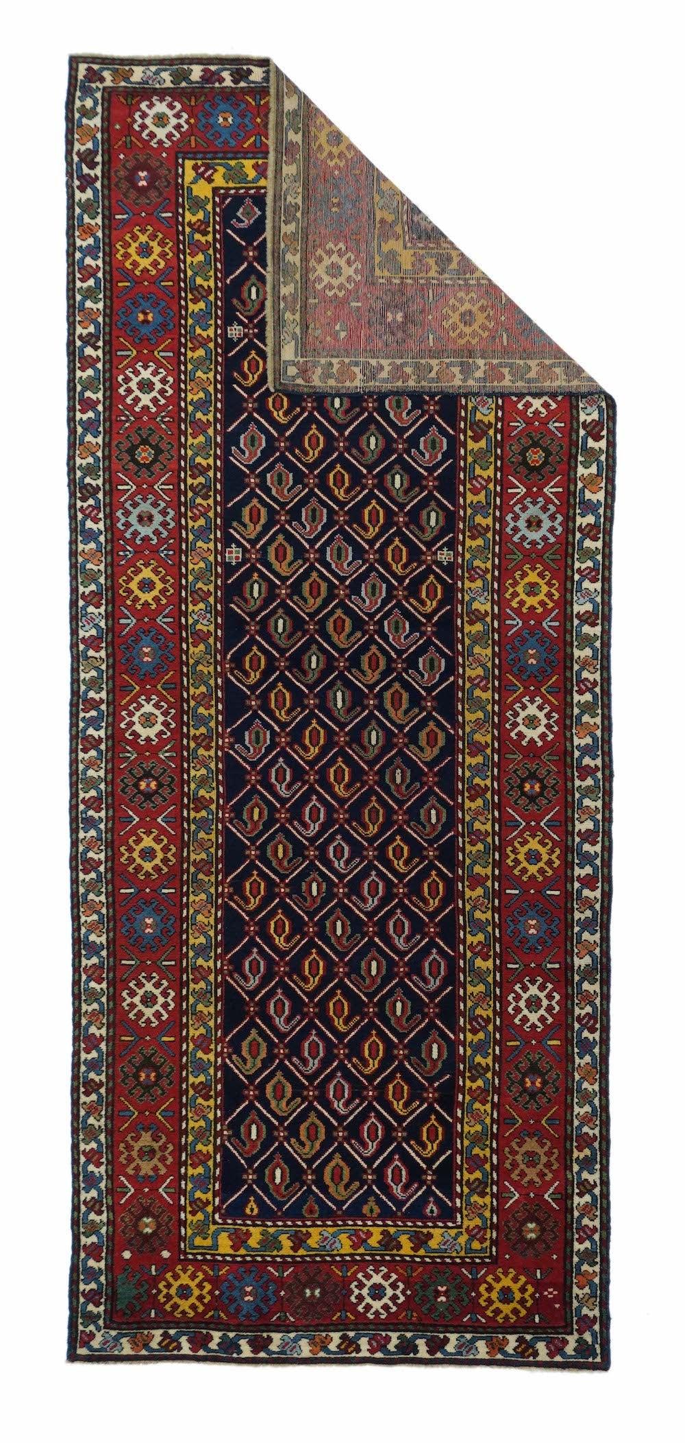 From the southern Caucasus, this good condition long piece presents a dark indigo blue field decorated with a diamond lattice enclosing row by row reversing botehs, but all in one general direction. Madder red main border with ivory, yellow, near