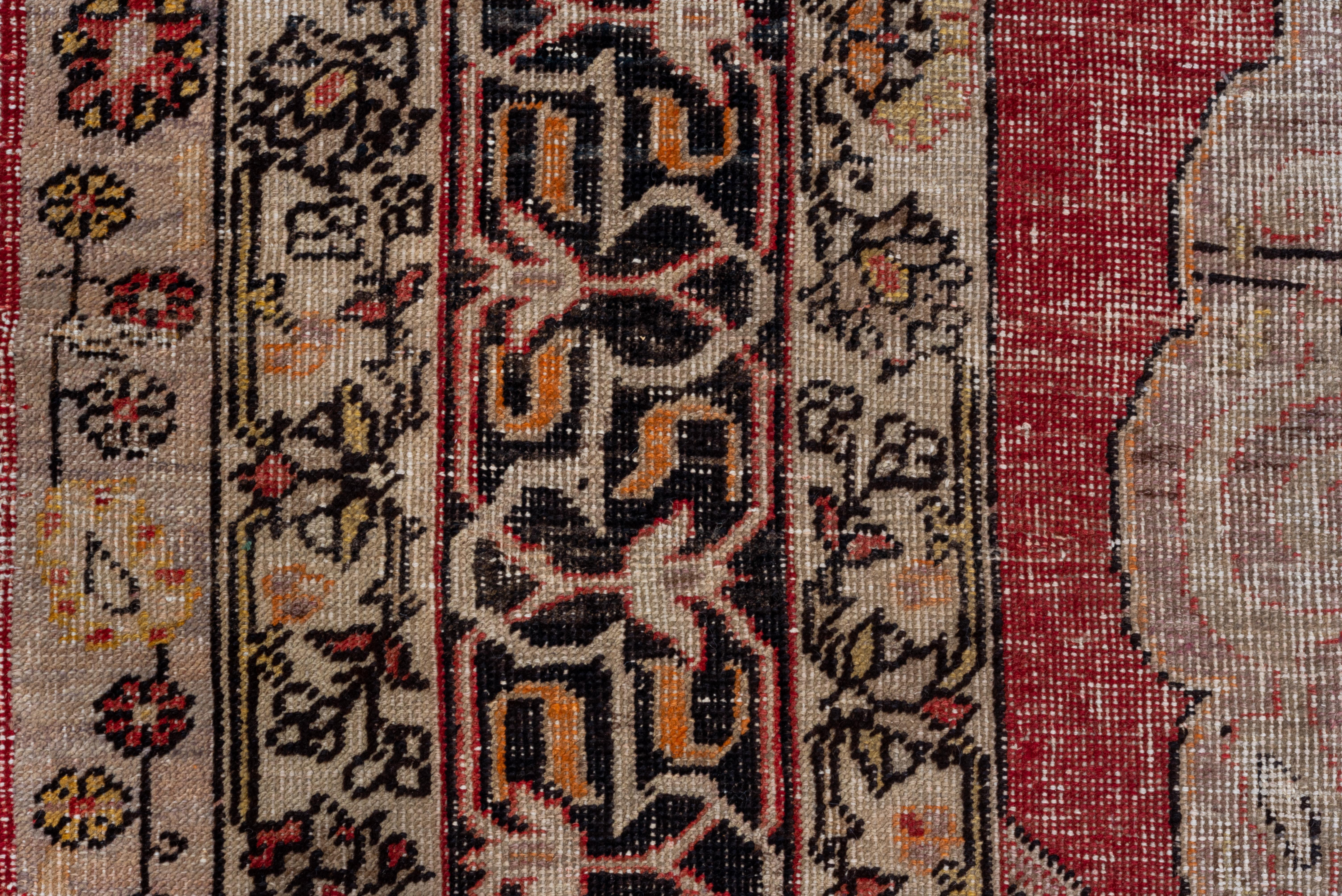 Although somewhat worn, this Oushak is better woven than most. The red field displays a giant ivory medallion with four scrolling field intrusions, giving the effect of giant blades. Cruciform palmette central motif in straw with enclosed palmettes.