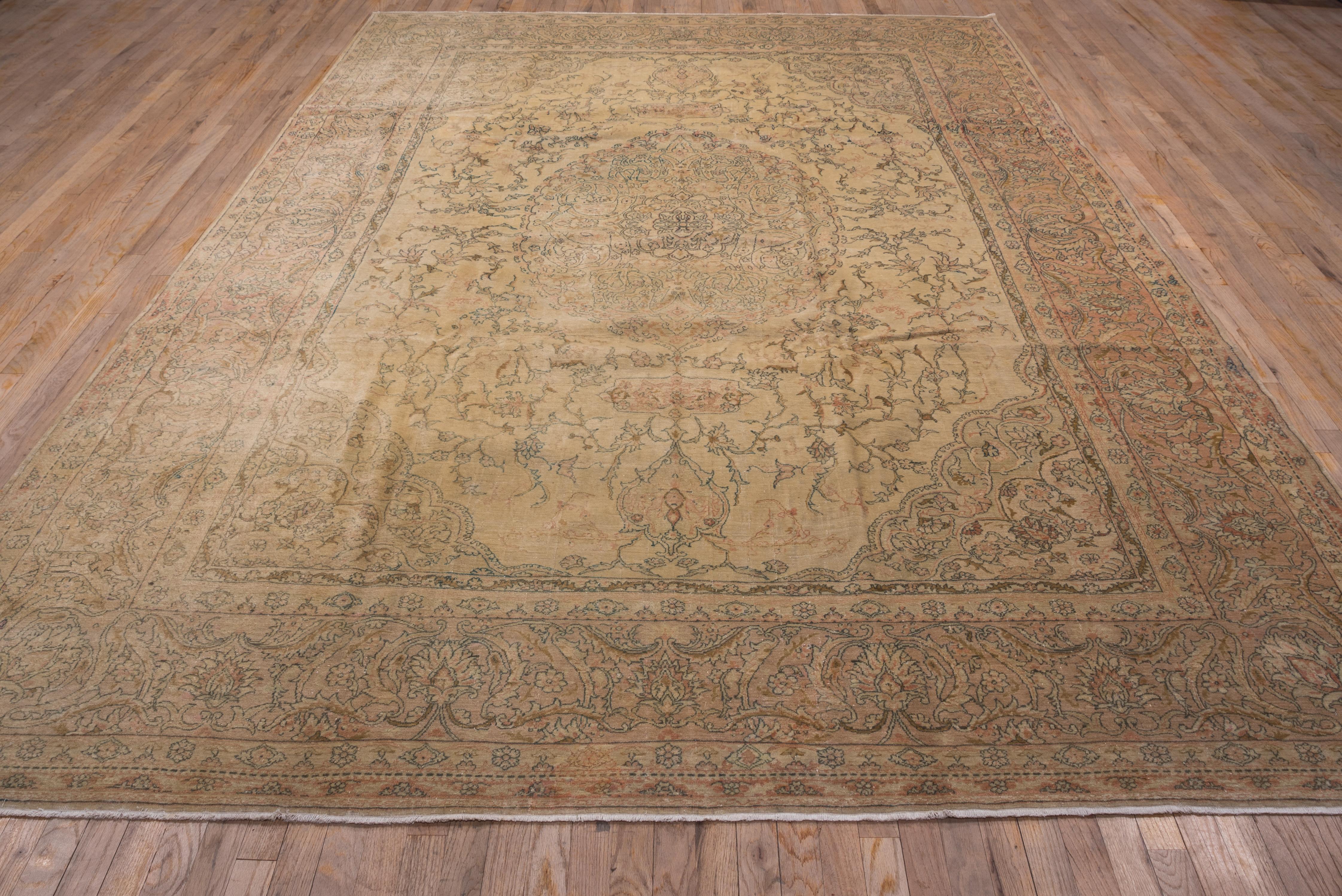In the Tabriz style, with a sandy straw field supporting a closely scalloped oval ogival medallion and roughly en suite corners. Doubled pendants. Stems bend and break around the medallion in the field. Ale buff-beige border with vigorous barbed