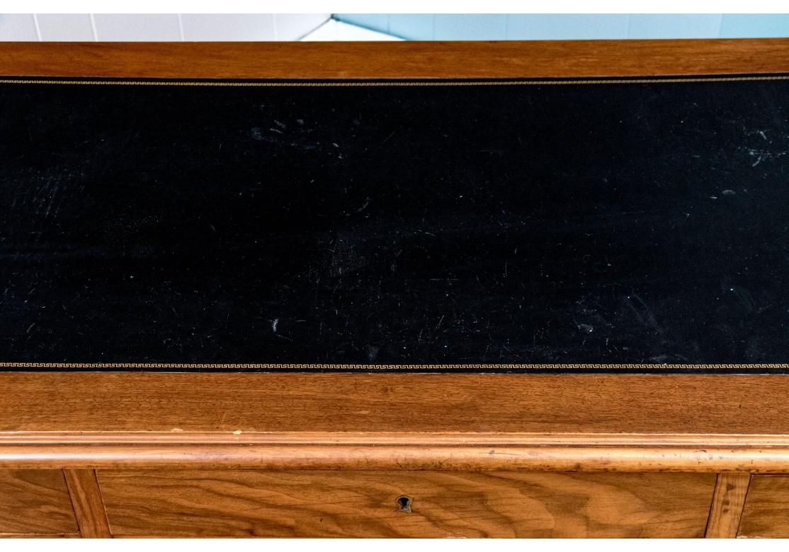 Bureau de style néoclassique à dessus en cuir, reposant sur quatre pieds tournés, effilés et cannelés, avec une caisse comportant un tiroir central, flanqué d'un tiroir à droite et de deux tiroirs à gauche. Les côtés du bureau sont dotés de retours