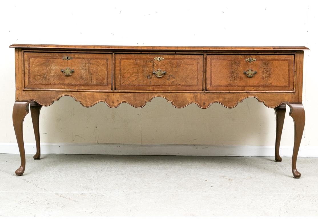 A classic Welsh sideboard in form, here in warm tone walnut. The rectangular top is constructed of book matched panels with a lighter center lozenge. It is also banded with additional herringbone string inlay and a carved edge. The case with three