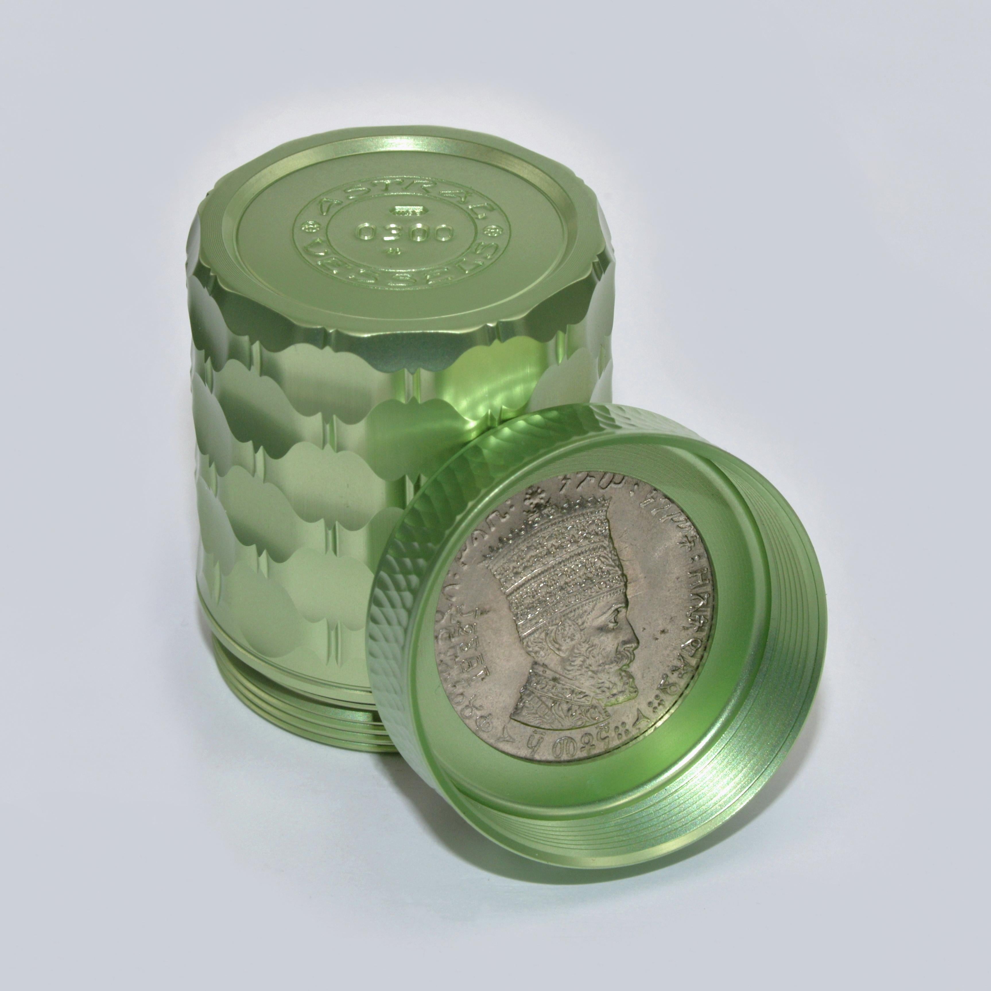A genuine Ethiopian 50 Matonas coin showing the triumphant Lion of Judah has been inset into the top. The obverse is visible on the inside of the cap, revealing the portrait of Emperor Haille Selassie II when the vessel is opened.
 
This sparkling