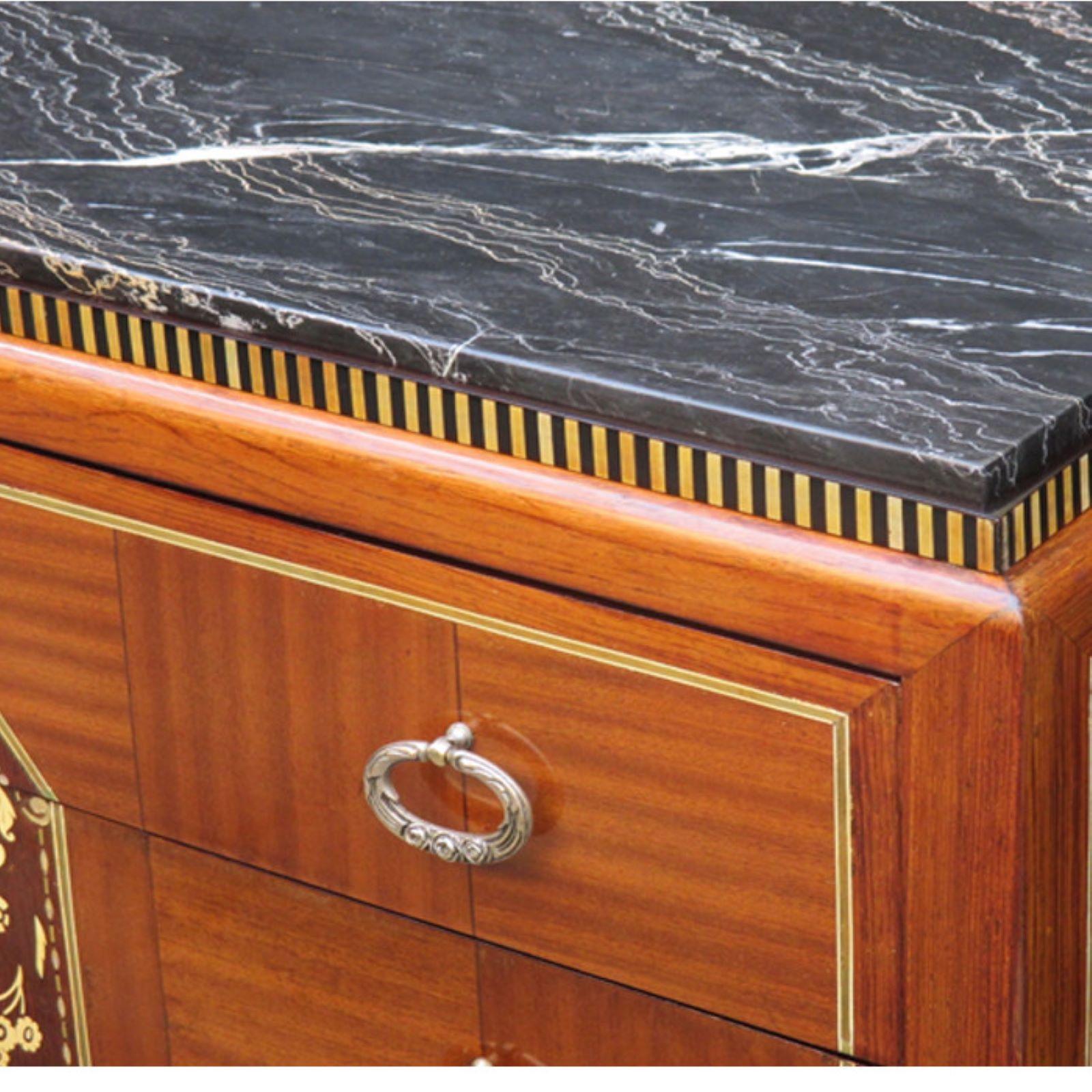 Importante cassettiera Art Déco. disegnata da DIM, René Joubert e Philippe Petit. Intarsio di mogano, intarsio di legno di frutta e di ebano, dettagli di intarsio in osso, dettagli delle gambe scanalate, tiranti in bronzo patinato e piano in marmo.