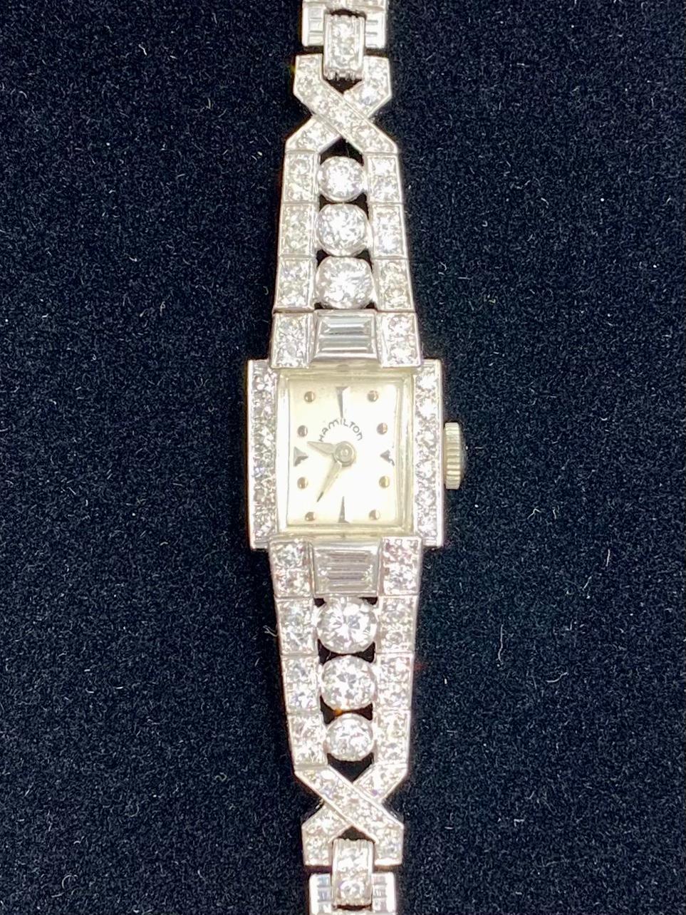 Elegante Hamilton Platin-Diamantenuhr aus der Zeit des Art déco mit 4,8 TCW und einem breiten doppelreihigen Platin- und Diamantarmband, stilvollen X-förmigen Diamantendetails und beträchtlichen Baguette- und Rundschliff-Diamantenakzenten.
Seit fast