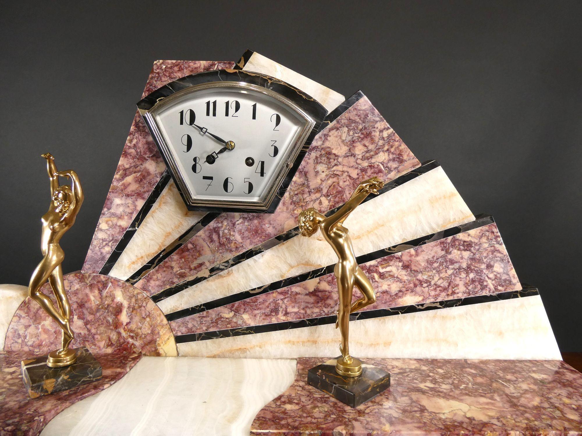 Fine Art Deco Marble Mantel Clock

Art Deco mantel clock housed in a fan shaped case with finely figured Rouge, Cream and Black marble inserts, standing on a stepped black marble plinth. The dial supported either side by two gilded dancers standing