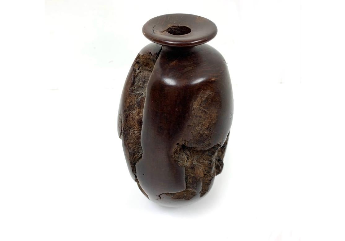 A fine natural burl wood sample carved into a bulbous tapering vase with a small opening on the flat rim. The vase is carved and partly polished leaving the natural rough features of the wood as part of the design. The flat base is covered with