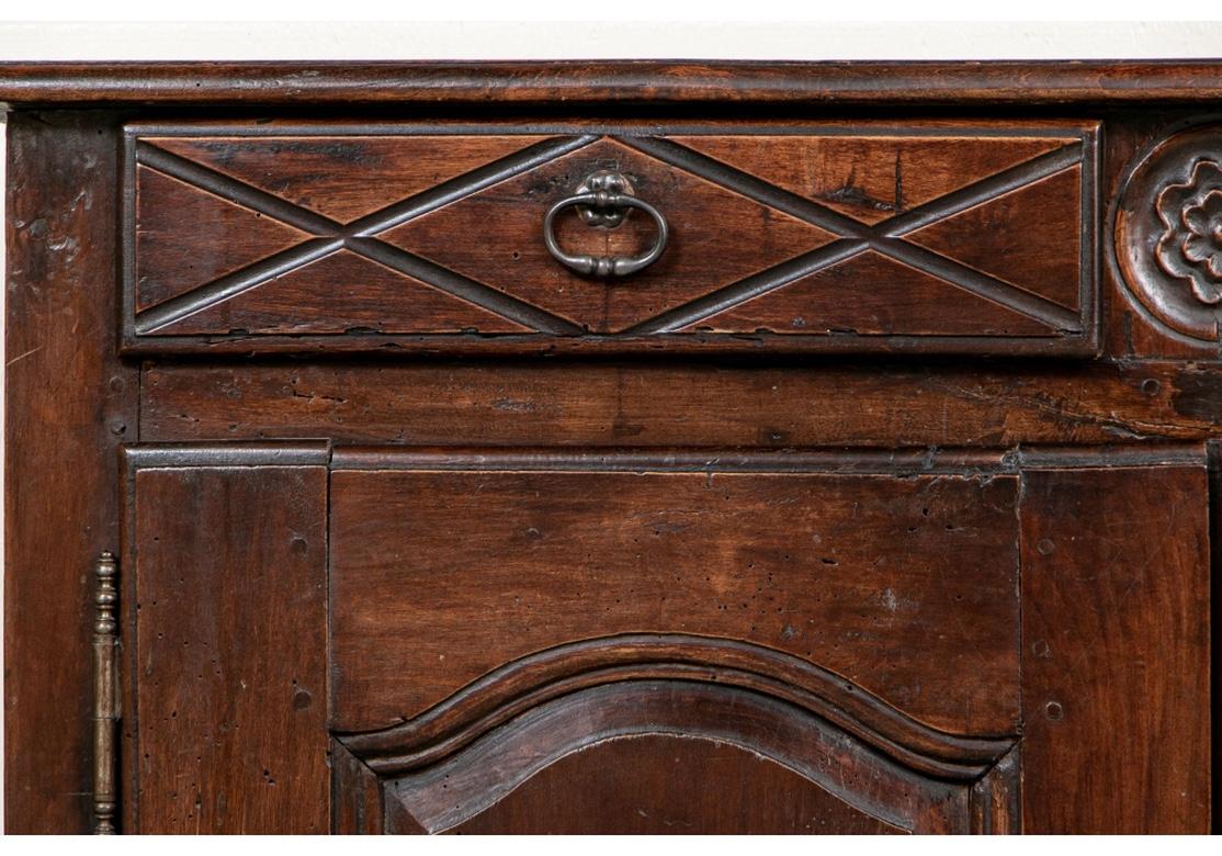 An early and authentic French cupboard in a dark stain, with a plank constructed top and recessed panel sides. The two carved frieze drawers flank a carved rosette. Carved double doors below over a scalloped skirt. A two part interior with shelves