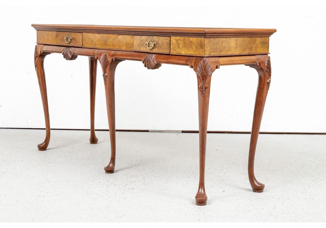 The top with a carved edge and mahogany panels banded in figured wood. The frieze in figured wood with two short drawers in front. A lower mahogany frieze with carved shells, raised on elegant cabriole legs with carved palmettes on the knees and pad