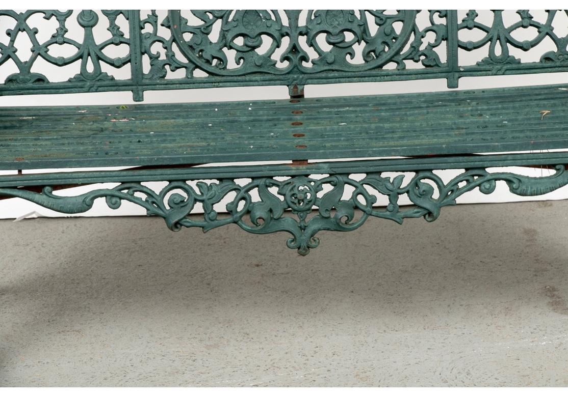 A very fine iron bench in Belle Époque style. The iron bench in old green paint, worn in places to reveal older white and red paint. With an elaborate openwork arched back with center fan and trefoil motifs, flanked by leafy motifs. The sides, skirt