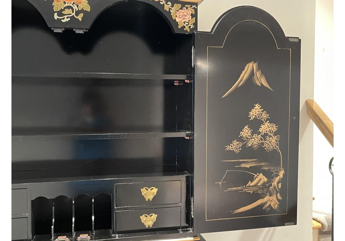 A black lacquer chinoiserie secretary in two parts. The upper cabinet with two doors that open to reveal 2 shelves, 4 pigeon holes flanked by small drawer with butterfly form hardware. The lower cabinet with drop down door with additional pigeon