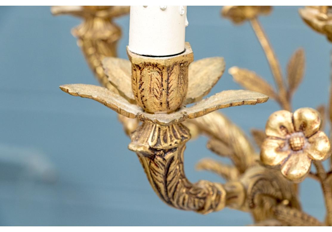 Un piccolo e decorativo motivo floreale in ottone. Lampadario. Il lampadario vintage a cinque luci è realizzato in ottone con due livelli decorati con fiori sporgenti a gambo lungo. I dettagliati bracci a voluta sostengono le luci con prese e