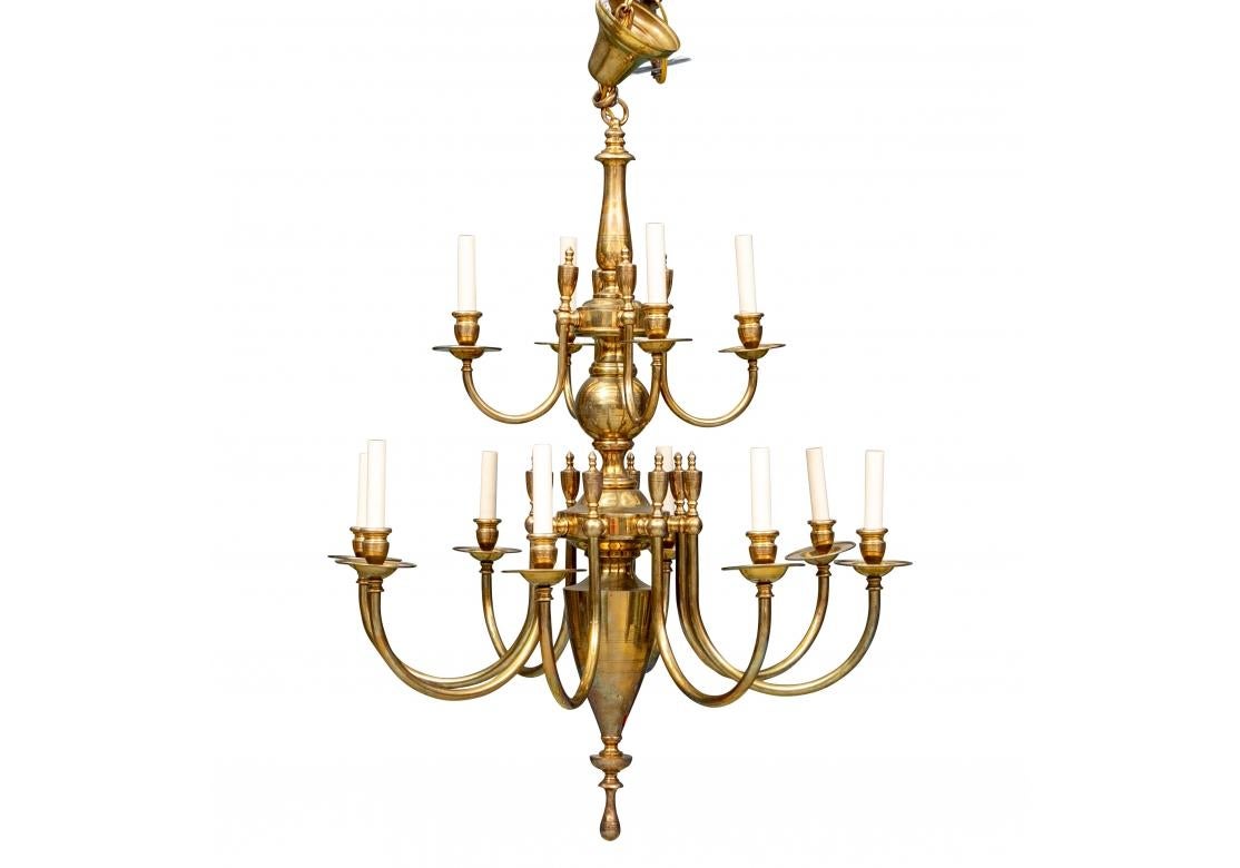 A handsome and larger brass chandelier in an elongated traditional form. The top with a baluster form standard and a center bulbous segment for the four arched lights with bobeches and vasiform finials. The lower tier with eight arched lights with