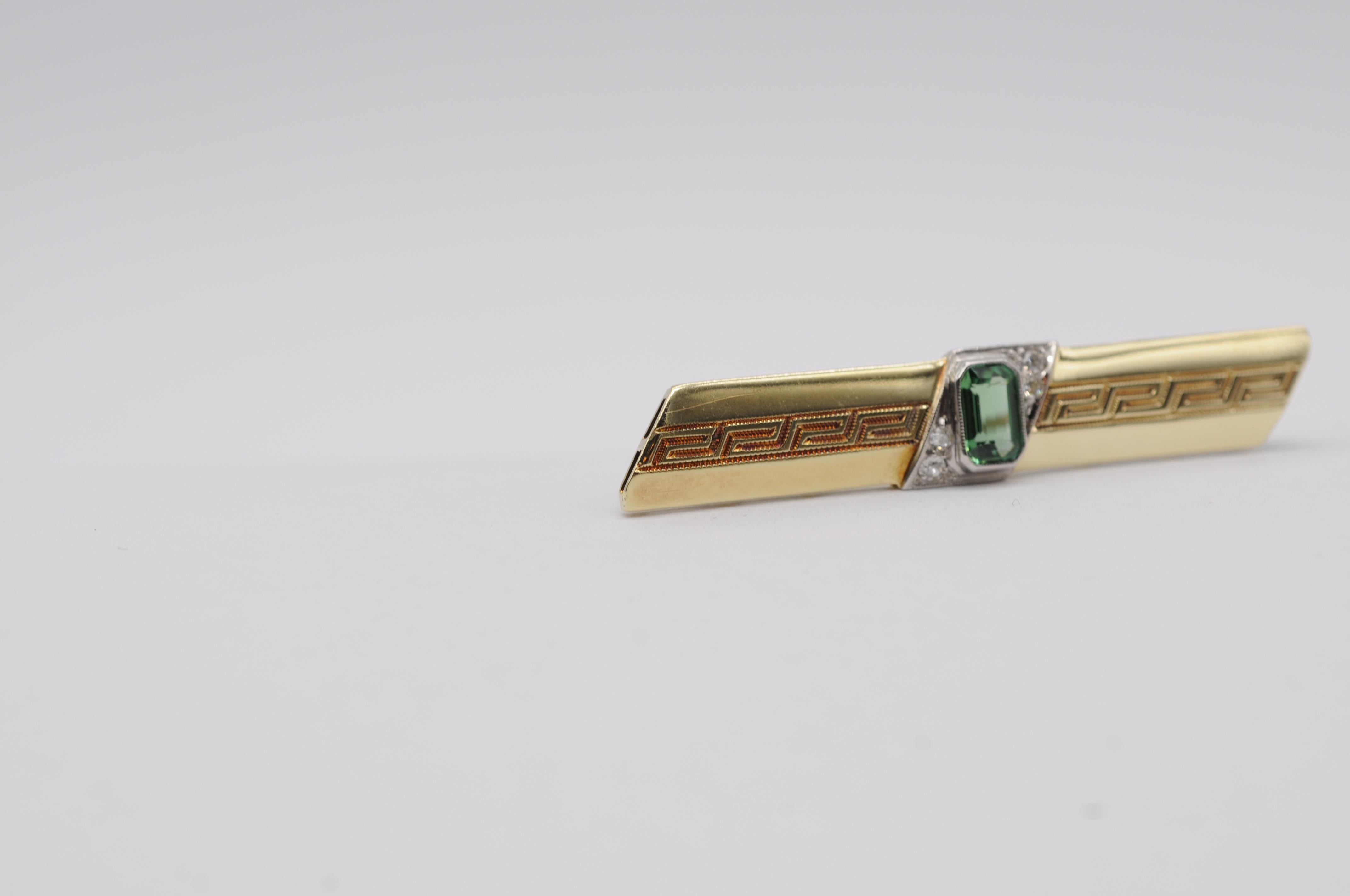 Presenting an exquisite piece of jewelry, a breathtakingly beautiful 14k yellow and white gold brooch. At its center rests a stunning green tourmaline, approximately 0.70 carats, expertly cut into an elegant emerald shape. Surrounding this