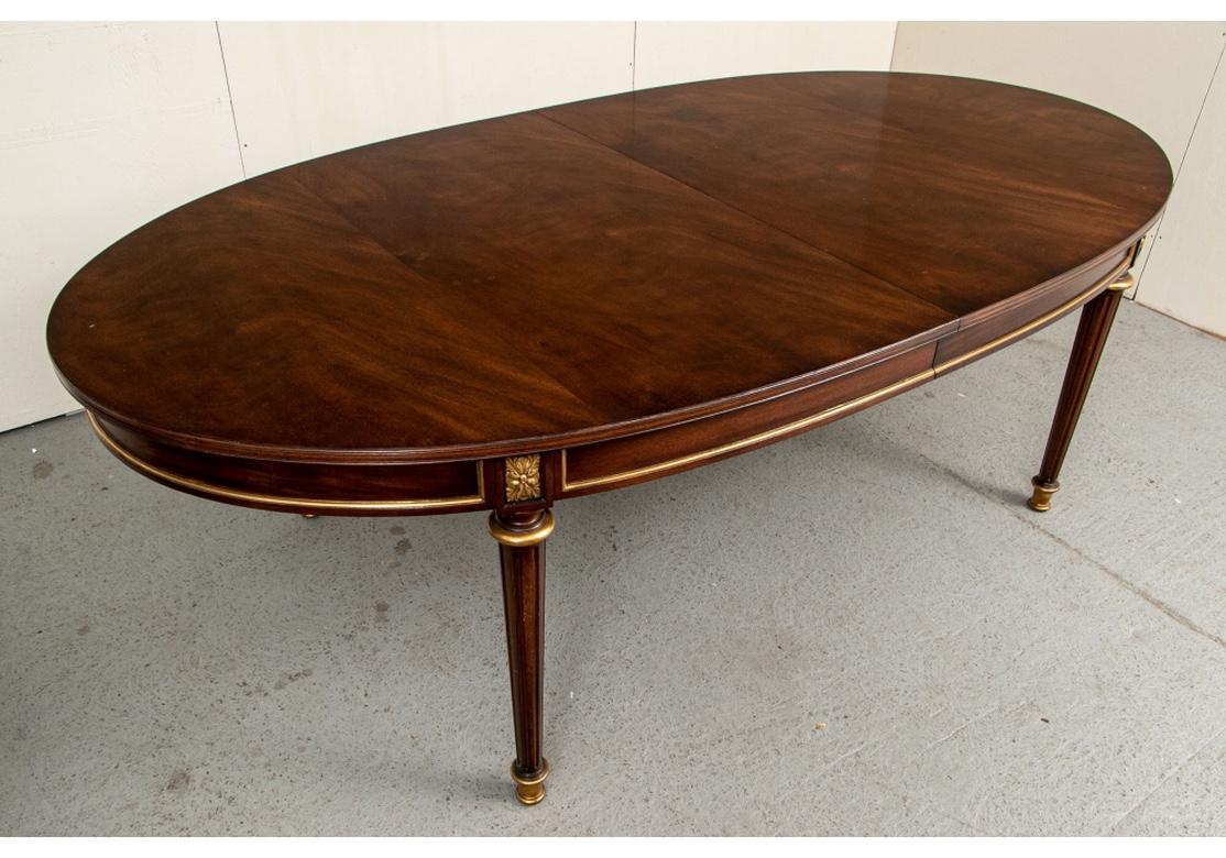 An oval table with very fine classic Directoire form having fluted column legs with gilt details and gilt leafy panels and edges on the frieze. The table is all wood and very sturdy, the leaf sliders are oak. There are three 24” leaves held in a