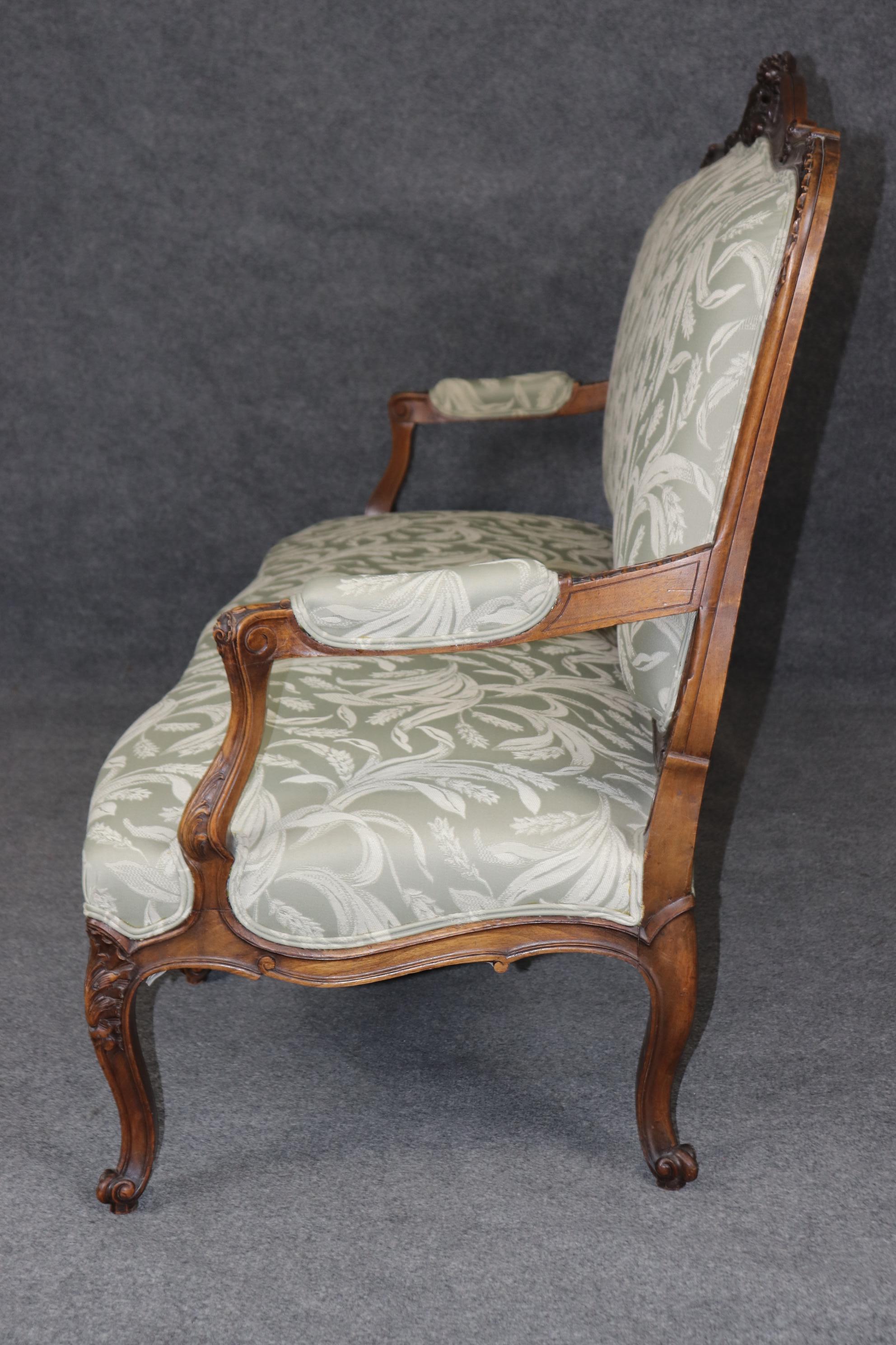 This is a superbly carved French Louis XV style walnut sette or canape. The settee is in very good condition for its age with a fine original finish and nice, clean older upholstery. The settee is precisely hand-carved and has wonderful details. The