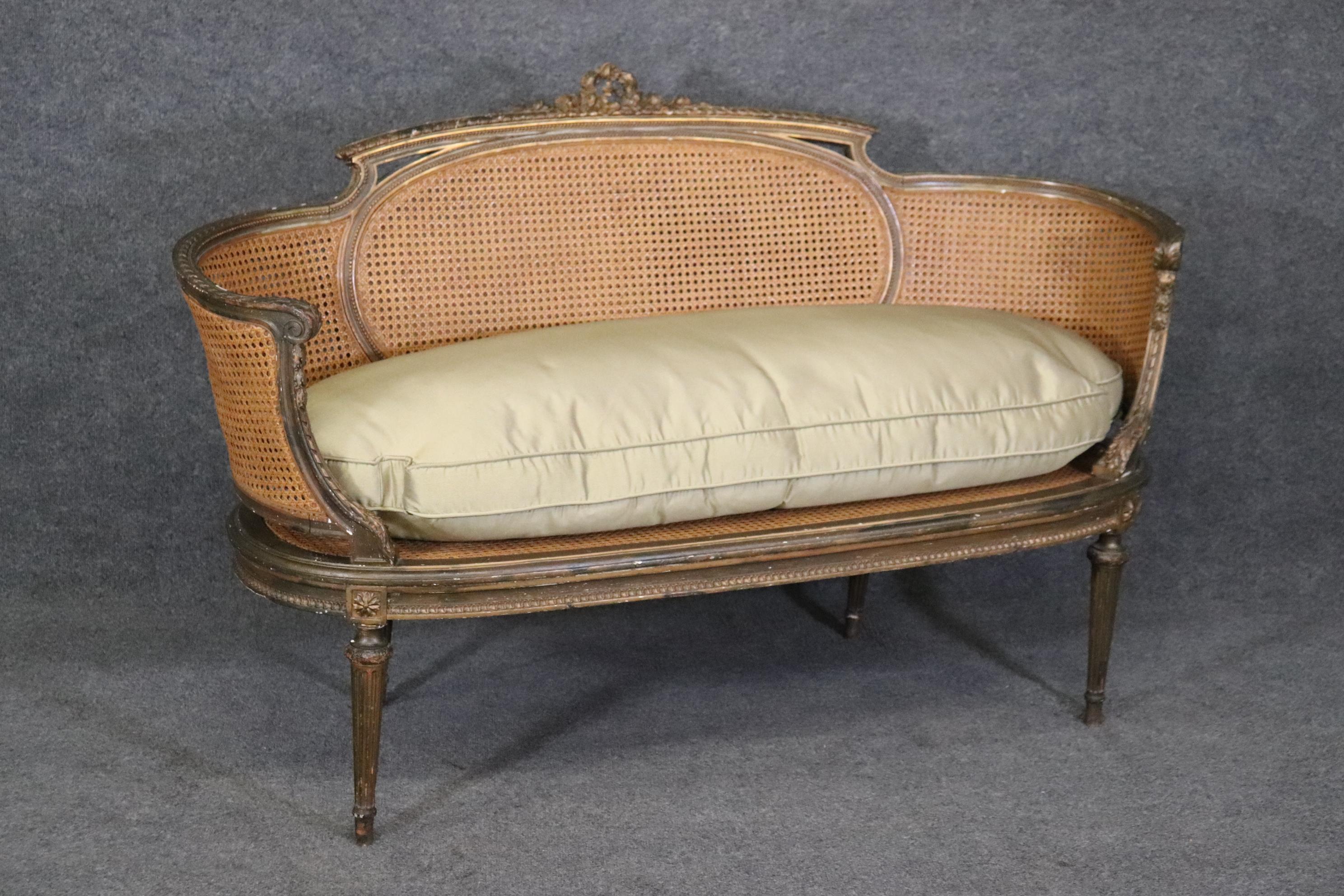 This is a wonderful settee with a curved frame and beautiful caned back. The settee is done in an antique bronzed gilded finish and is in good condition with wonderful carving and a great cushion that appears to be silk. The piece measures 36.75