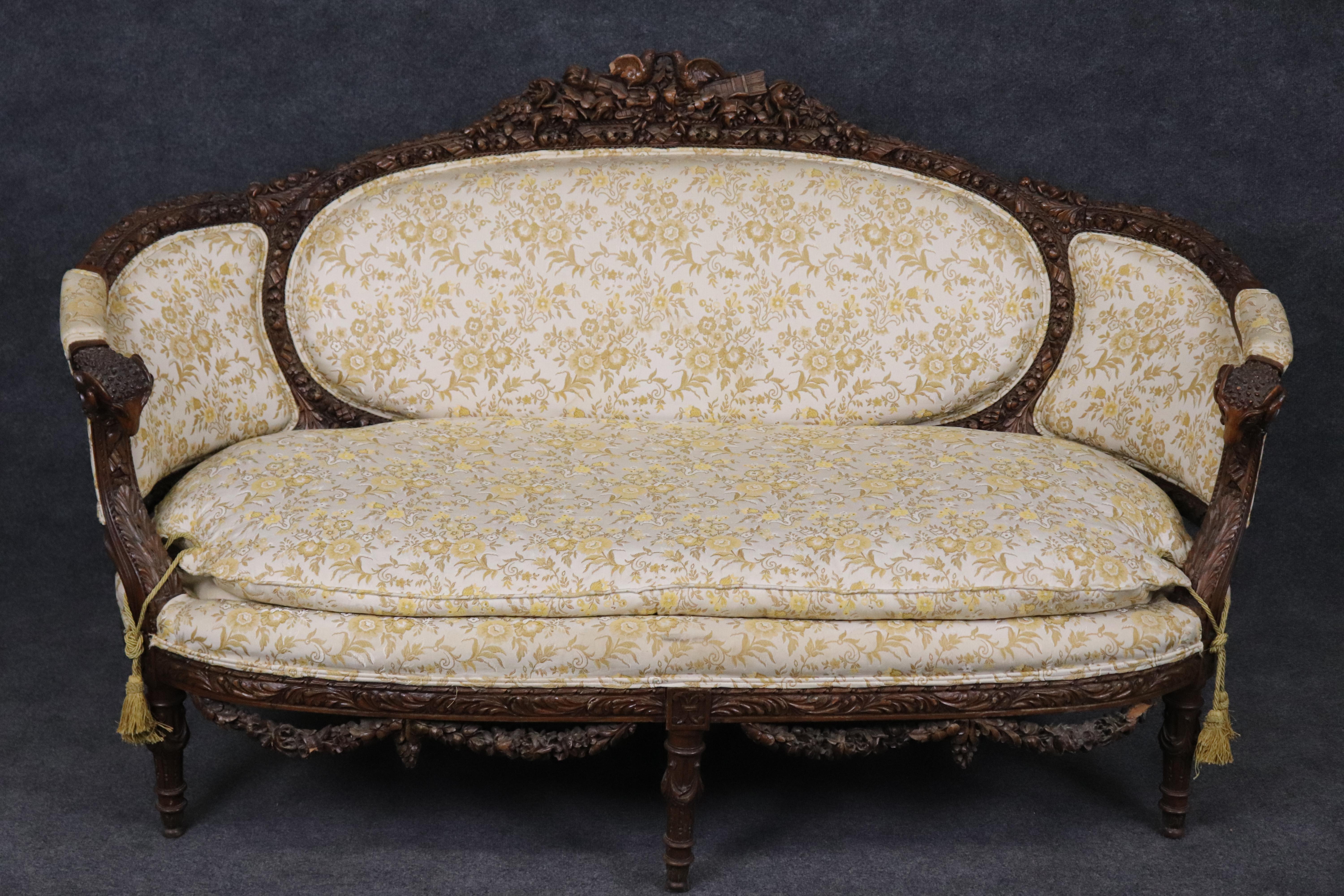 This gorgeous sofa features meticulously carved Kissing birds and gorgeous garlands of flowers and full carved ram's heads at each arm. The sofa is solid carved walnut and features its original finish and older vintage upholstery. The piece is in