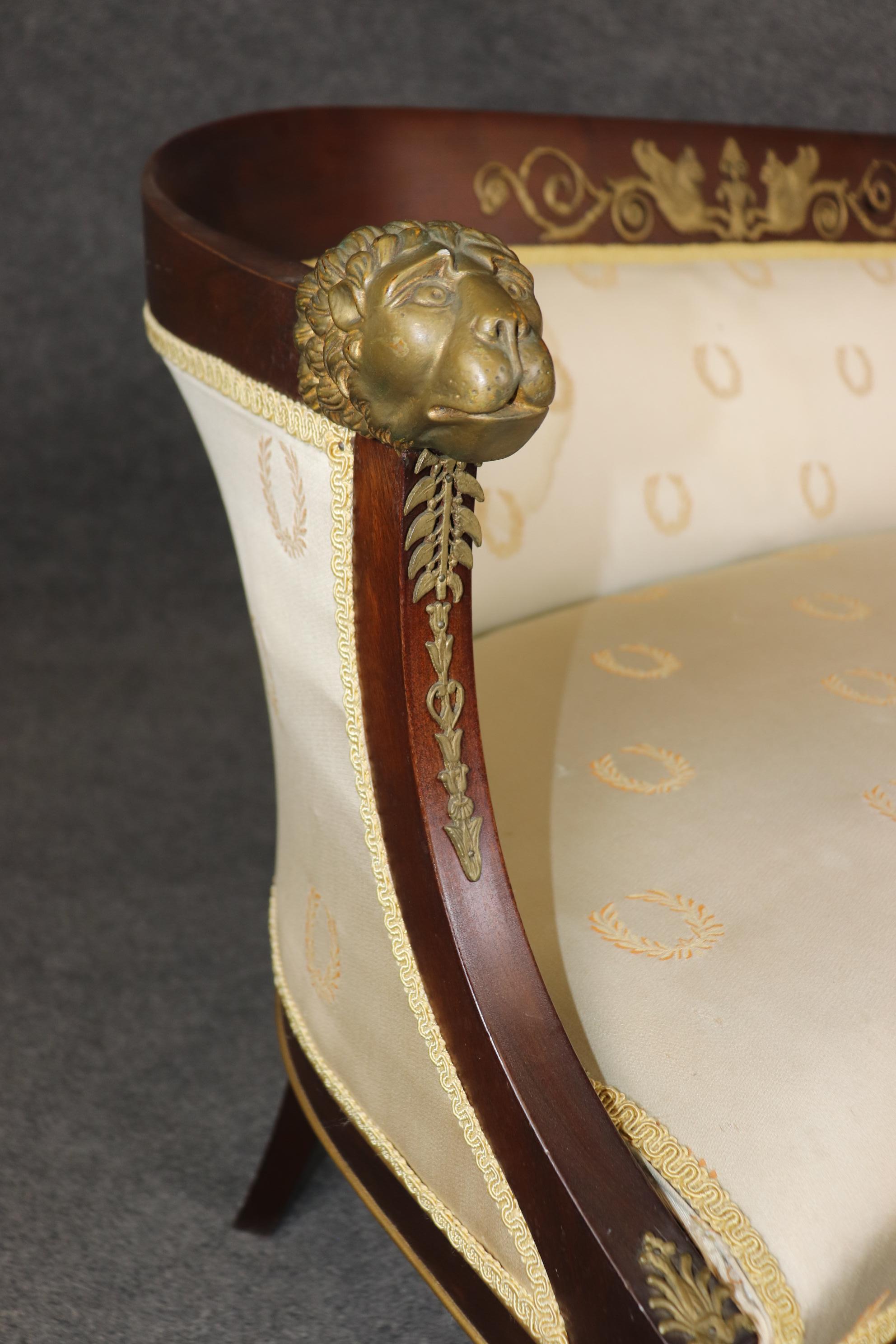 This is a unique French Empire style settee. Made in France during the 1920s it wears an old New York upholstery tag but is French. The piece features unique dog faces cast on the terminals of the arms and dragons on the very top of the back as well