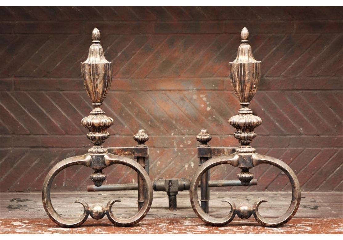 Very fine pair of silver-plate andirons in very good condition with exceptional form. With ribbed urn form finials, mounted on tiered bulbous stands and scrolled bases. The shaped ends at back with bulbous finials. Iron bars at back. 
Condition: