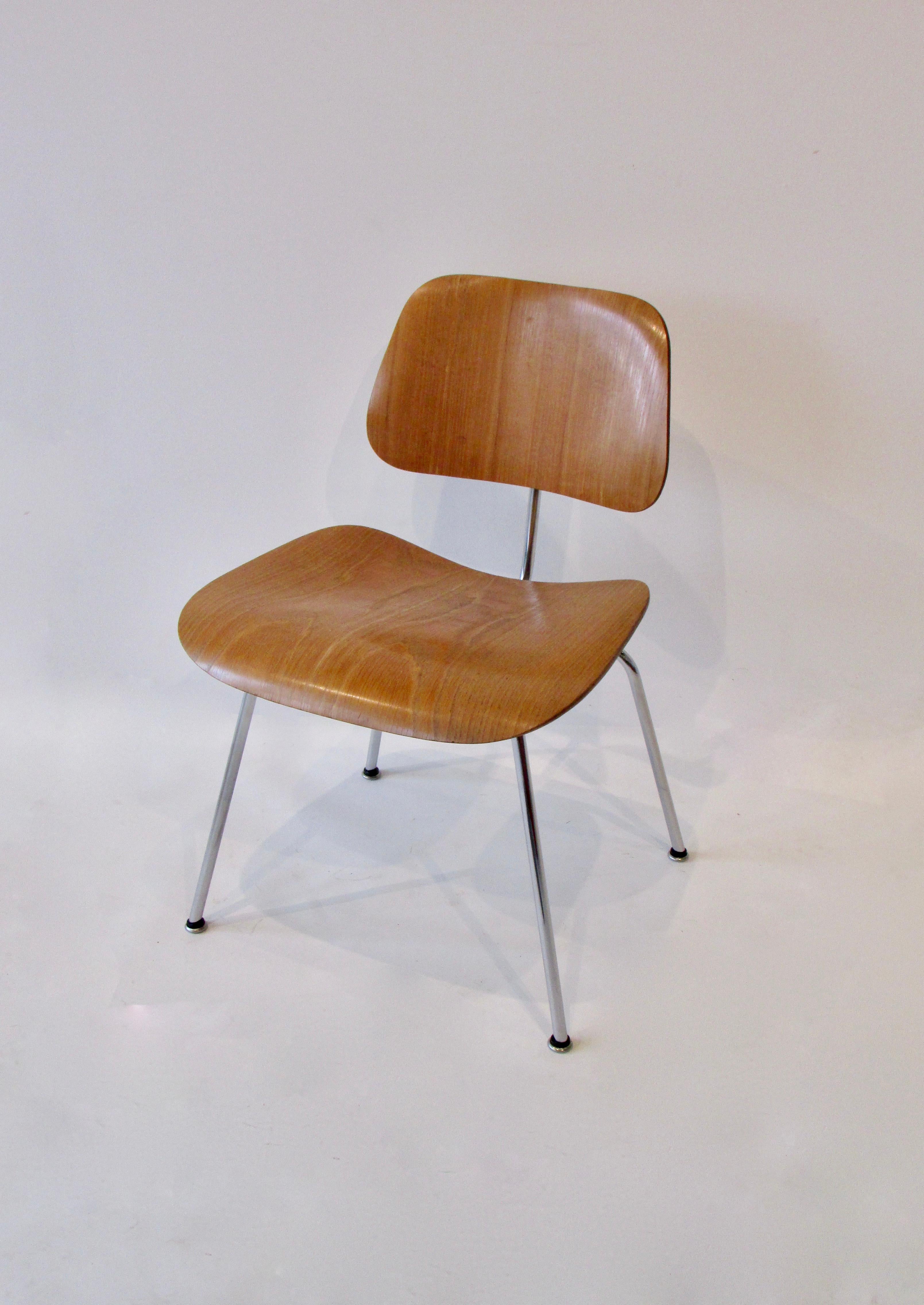 Silla de comedor de metal (DCM ) diseñada por Charles and Ray Eames, muy bonita y de producción temprana. La limpia estructura cromada soporta el asiento y el respaldo de fresno veteado. Conserva la etiqueta original de la calcomanía al agua Eames