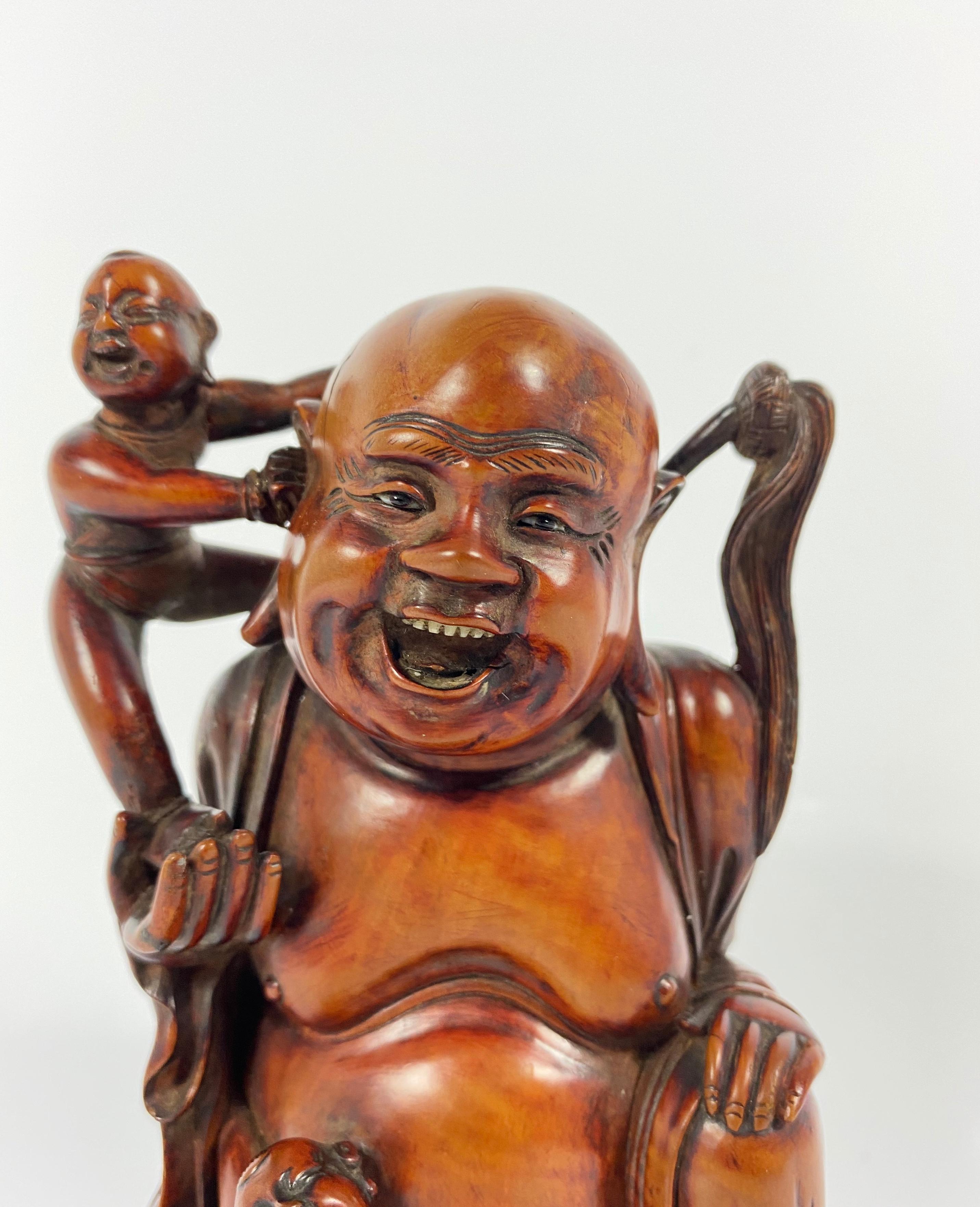 An exceptionally fine Chinese hardwood figure of Buddha and the He He Erxian twins, 19th century, Qing Dynasty. Beautifully, and amusingly carved as Buddha, seated cross legged, and with an amused expression, whilst the twins attend to him. His face
