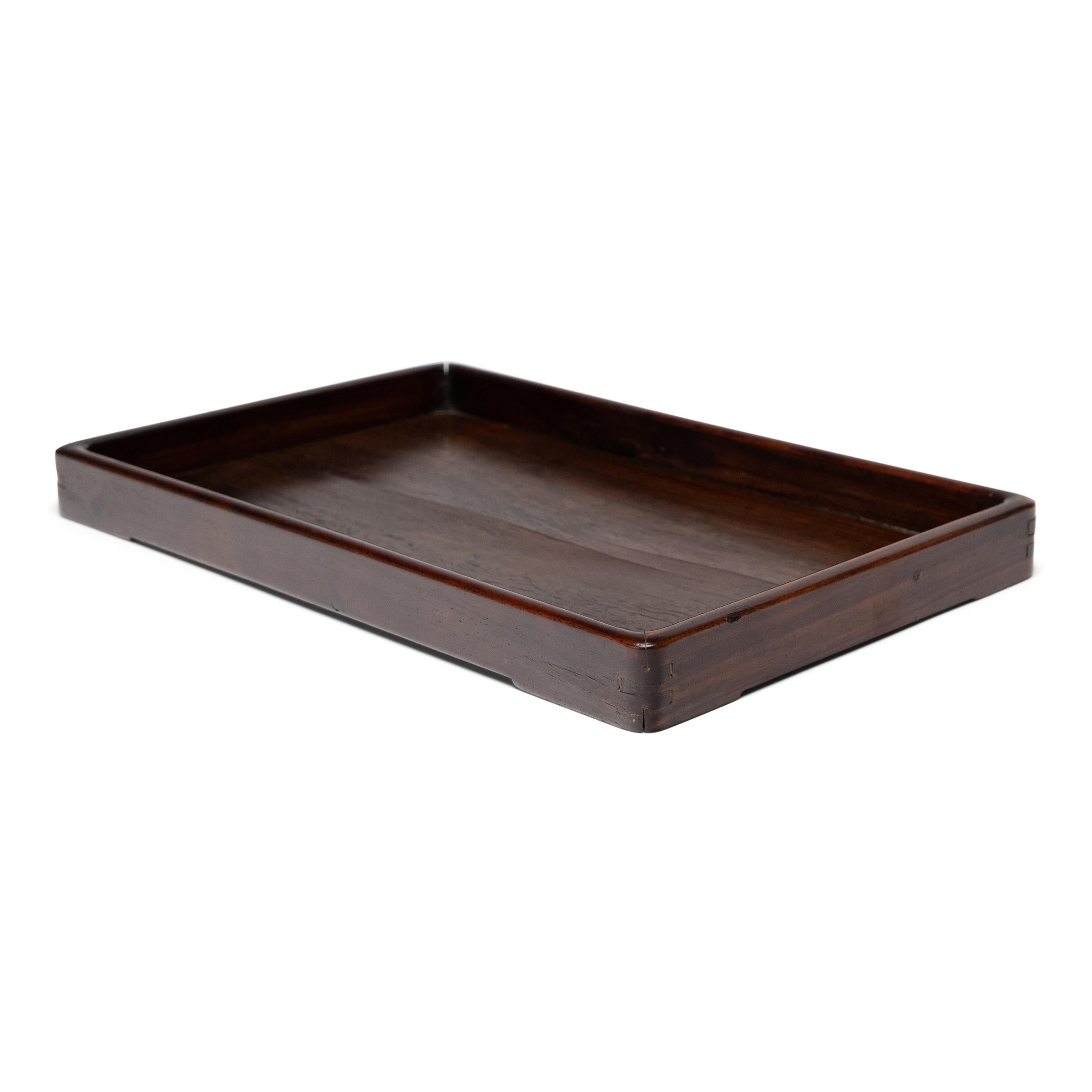 This 19th-century serving tray exemplifies Qing-dynasty refinement with simplicity of form and an emphasis on natural materials. Crafted of a darkly colored hardwood, the elegant tray would have been used for serving tea, storing opium accessories