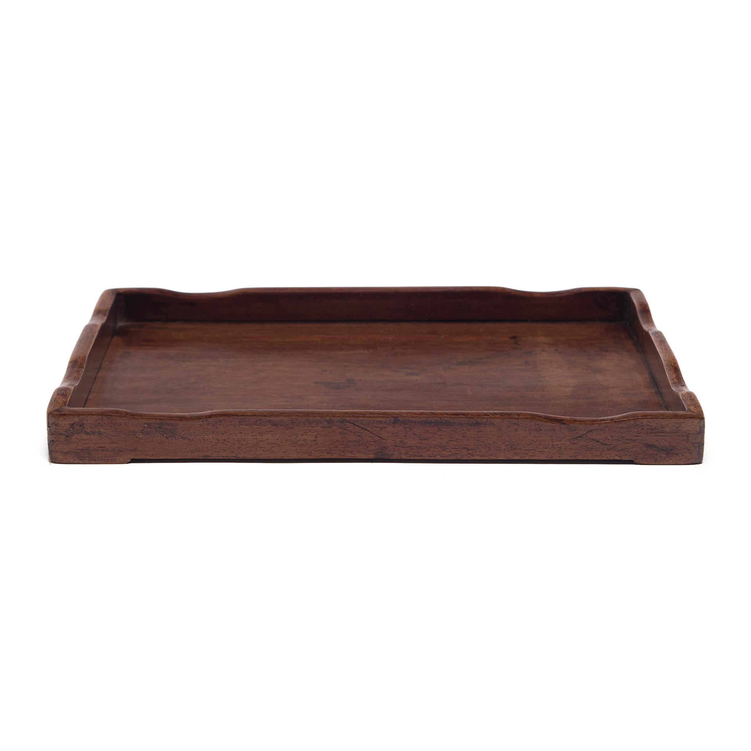 Crafted of fine hardwood, this 19th century tray once served tea or displayed calligraphy tools in a scholar's studio. Framed by low, curved sides, the tray has a simple rectangular form that showcases its rich color and fine wood grain.