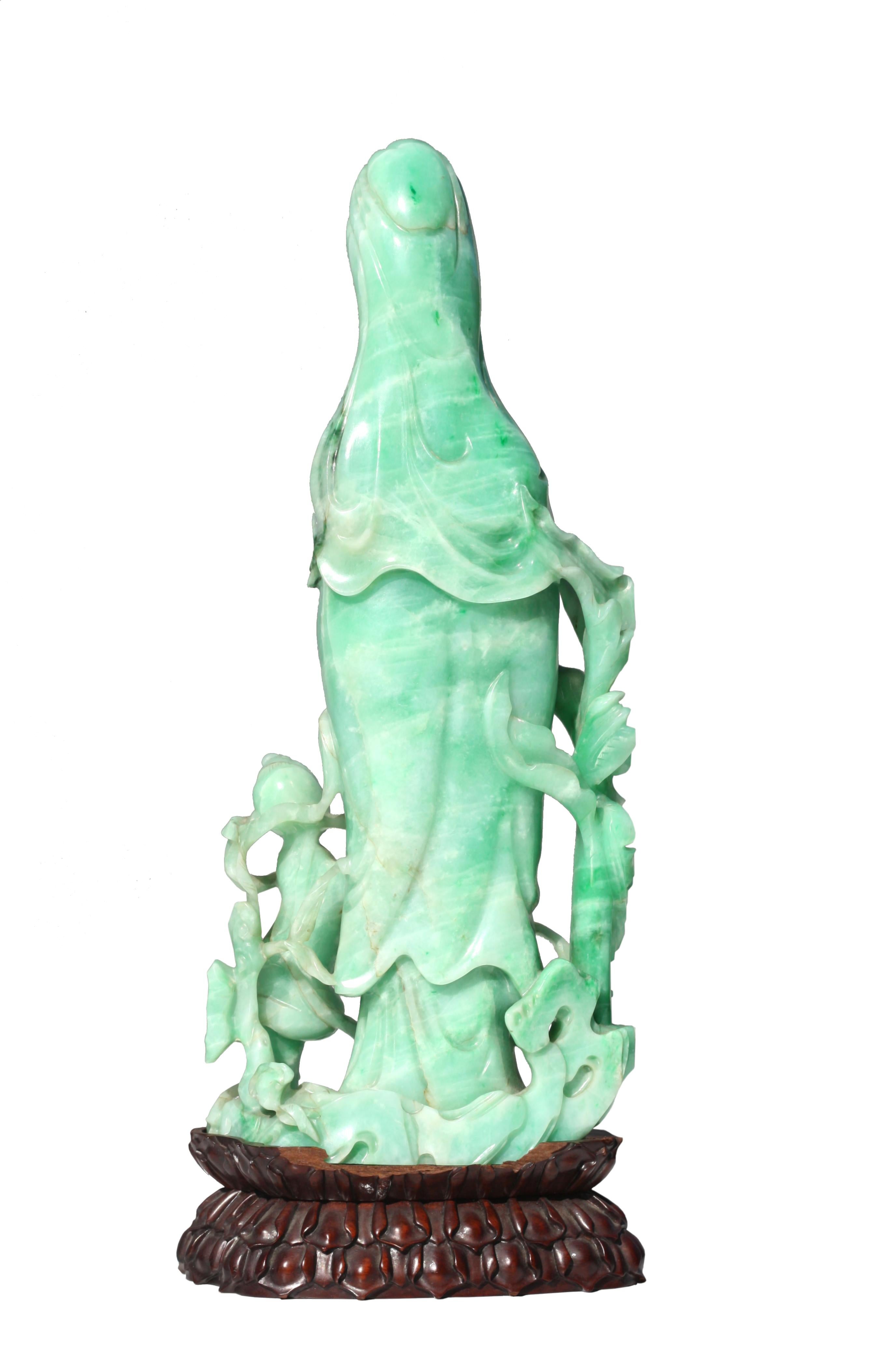 
Fine Chinese Emerald Green Jadeite Quanyin
The standing deity clothed in elegant robes, her hair coiffed in a knot and draped with a veil, her elongated face with a serene gaze, she holds a rod, by her side is a child, both standing amidst leafy