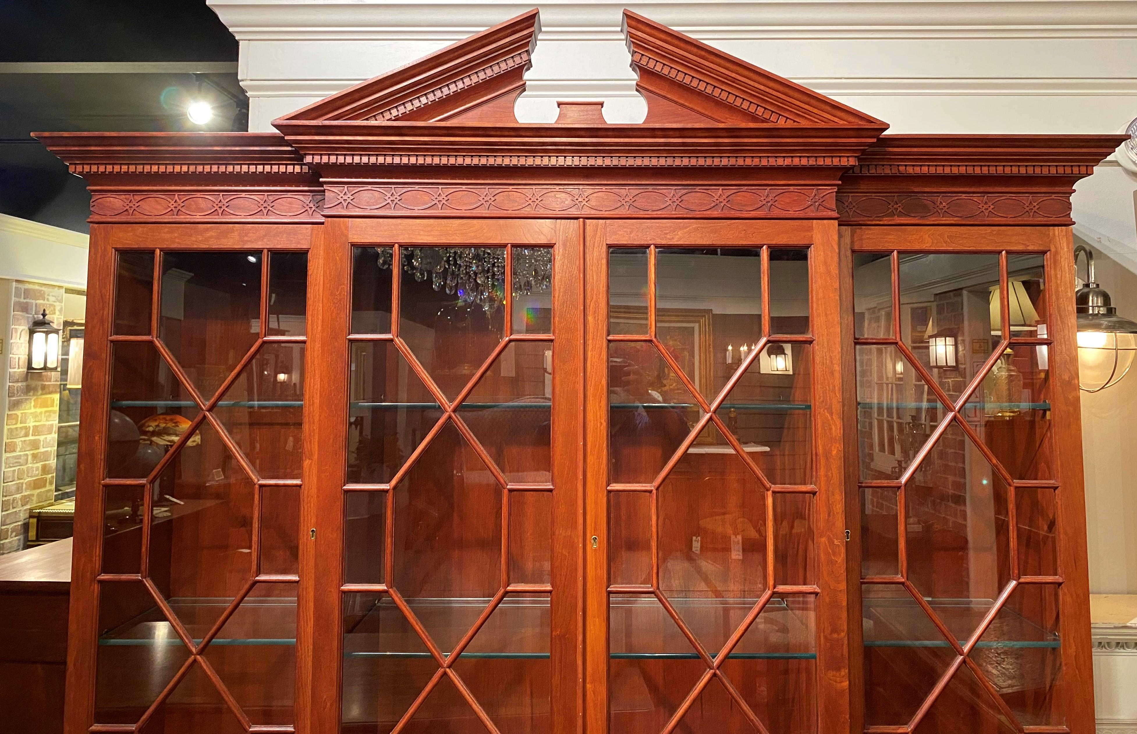 A fine quality Chippendale or Georgian style cherry two piece breakfront china cabinet or bookcase, the upper case featuring a split pediment crest and nicely carved cornice with dentil molding, surmounting four glass doors with fretwork opening to