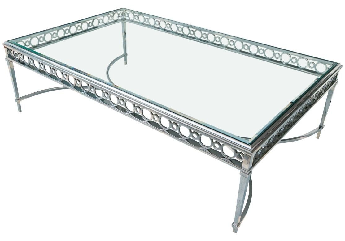 Cette table à cocktail en acier inoxydable chromé, bien construite, est équipée d'un plateau en verre. La table repose sur quatre pieds fuselés équarris, reliés à deux supports de brancard incurvés et gracieusement formés. La table présente un