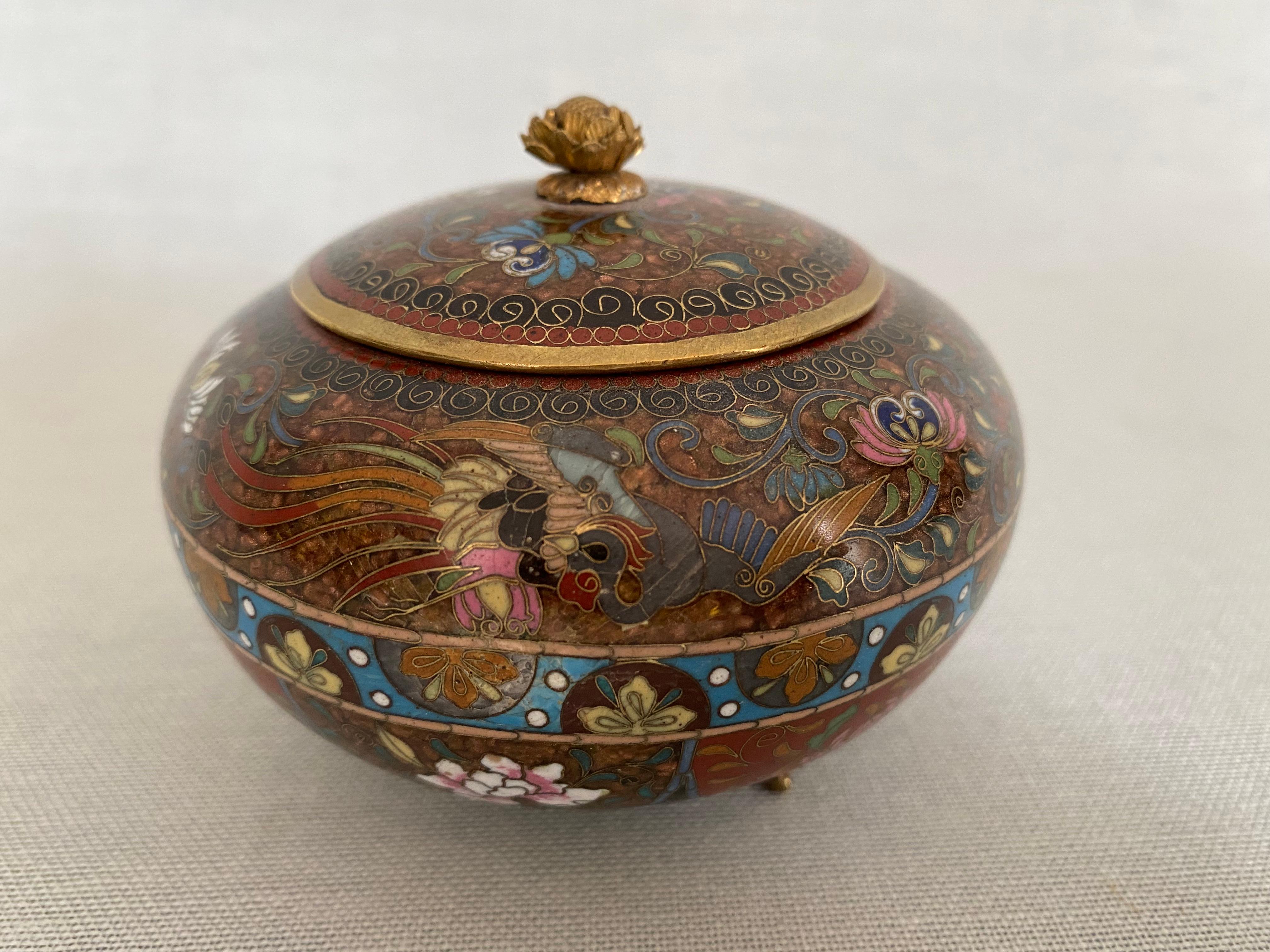 Fine Japanese cloisonne lidded box from the Meiji period. The small box stands on three brass feet. The lid, also made of brass, has a small flower as a handle that is just opening.
The box is richly decorated and finely worked out. A phoenix on a