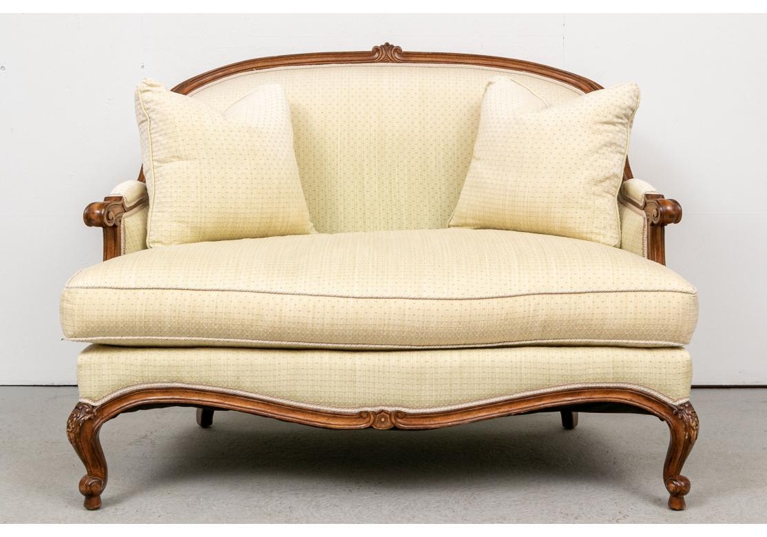 From Apropos, New York City. A Louis XV style tub form sofa with a carved walnut frame. The curved crest rail with a carved palmette as the crest. Scrolled arm ends and short carved cabriole legs with floral motifs in front, and curved square legs
