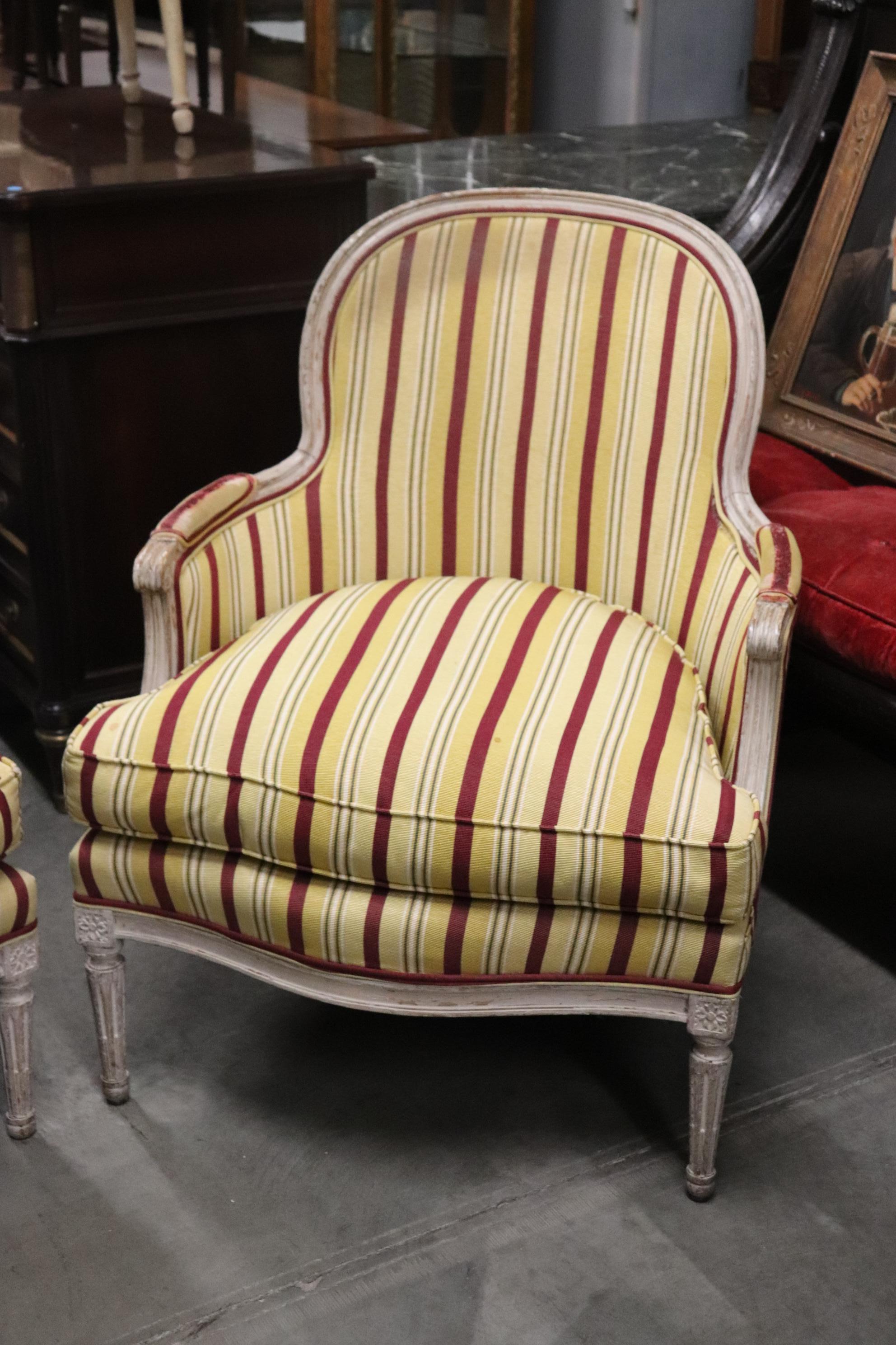 This is a gorgeous pair of distressed white pair of Louis XVI style bergere chairs. They are in beautiful yellow and red striped upholstery. The frames are just gorgeous and the upholstery, while not perfect, is very presentable and useable. They