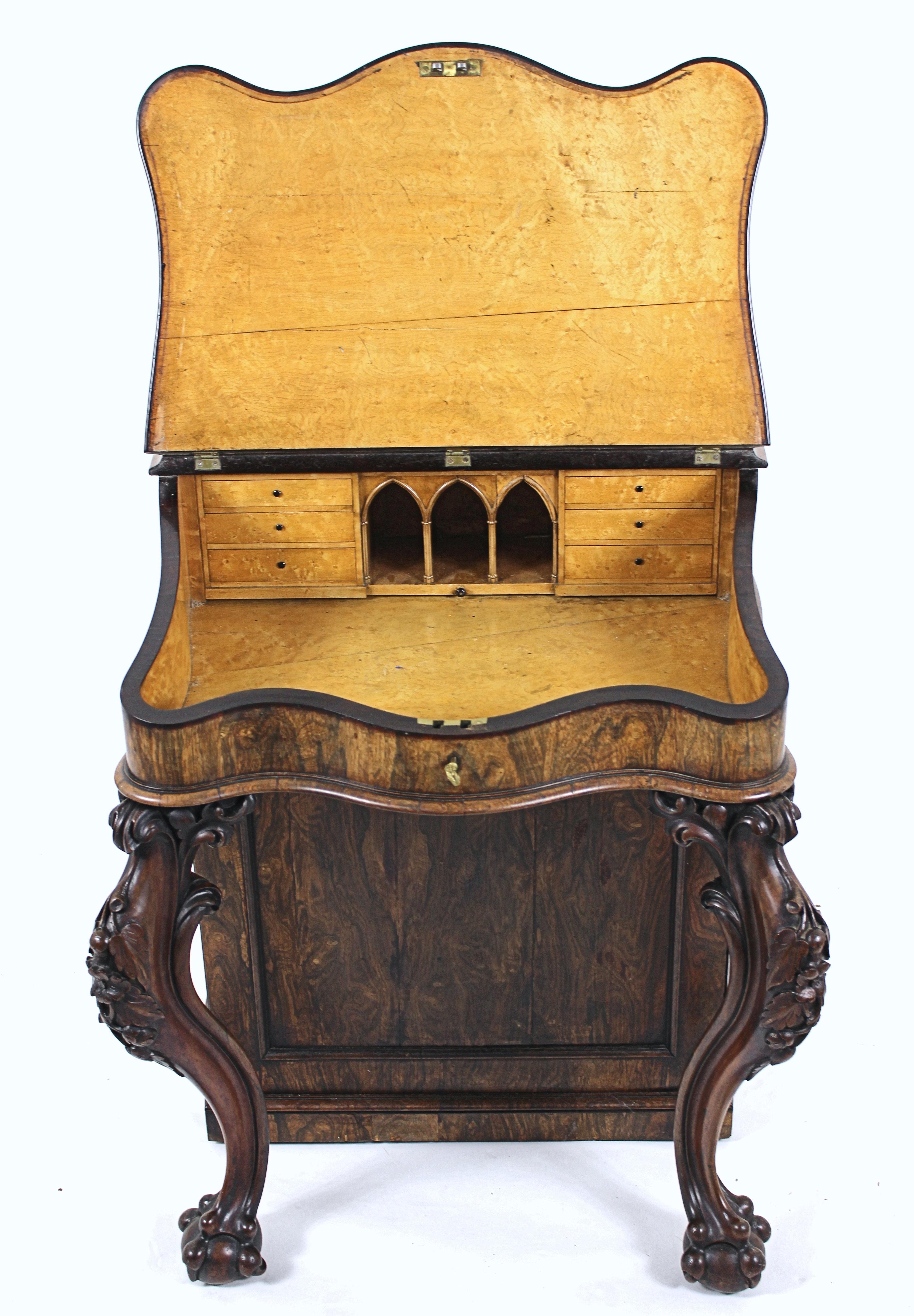 This outstanding and beautiful early 19th century. Irish carved rosewood serpentine shaped davenport features a rising top with a maple Gothic interior with bowed sides enclosing the drawers. The top has a detailed wooden spindle gallery and