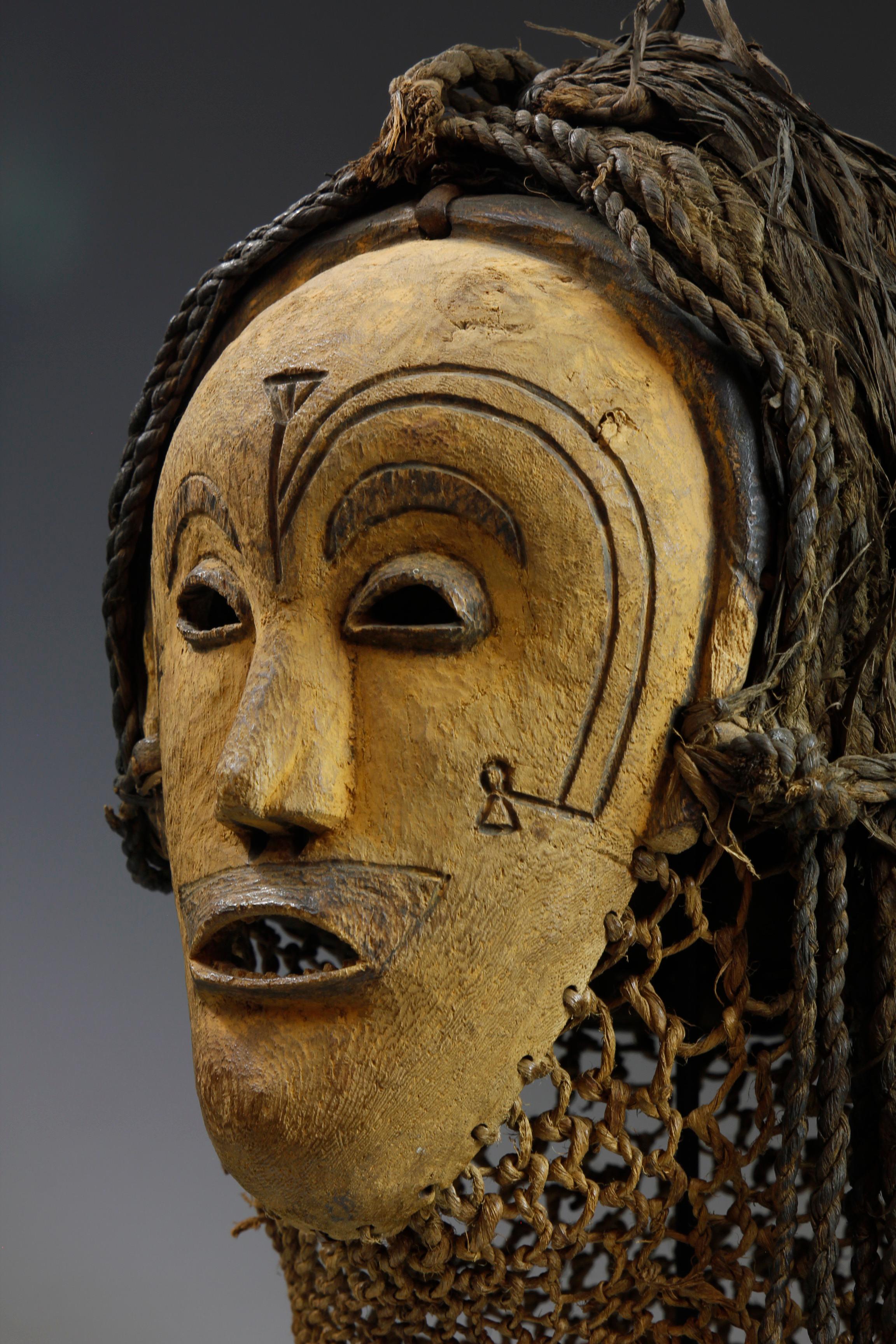 Diese Maske aus dem frühen zwanzigsten Jahrhundert aus der Chokwe-Kultur in Angola weist ungewöhnliche Merkmale auf. Die aus hellem Holz geschnitzte und mit gelben Pigmenten verzierte Maske weist seltene, in die Oberfläche eingebrannte Gesichtszüge