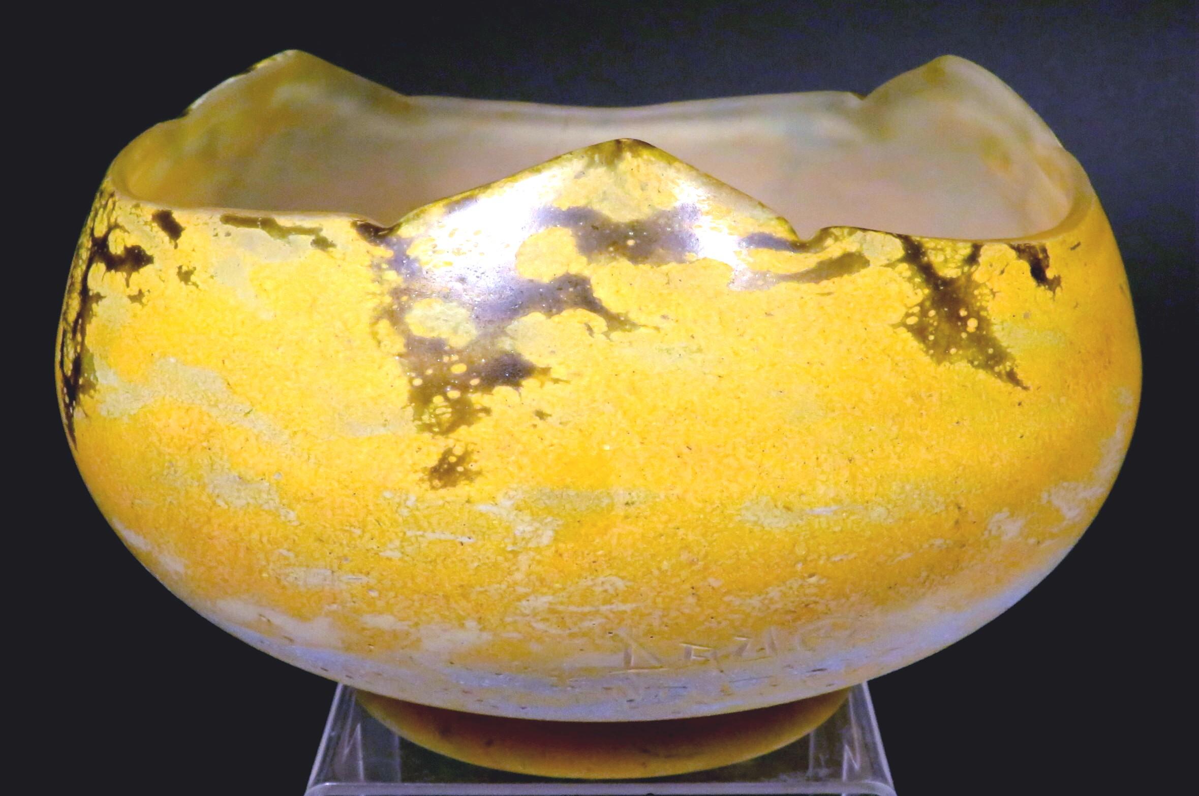 Il corpo circolare rigonfio mostra un campo caldo e screziato di giallo e marrone con striature verde acqua, che si innalza fino a un orlo a tre angoli e si solleva complessivamente su un piede circolare a gradini con un pontile a terra sul lato