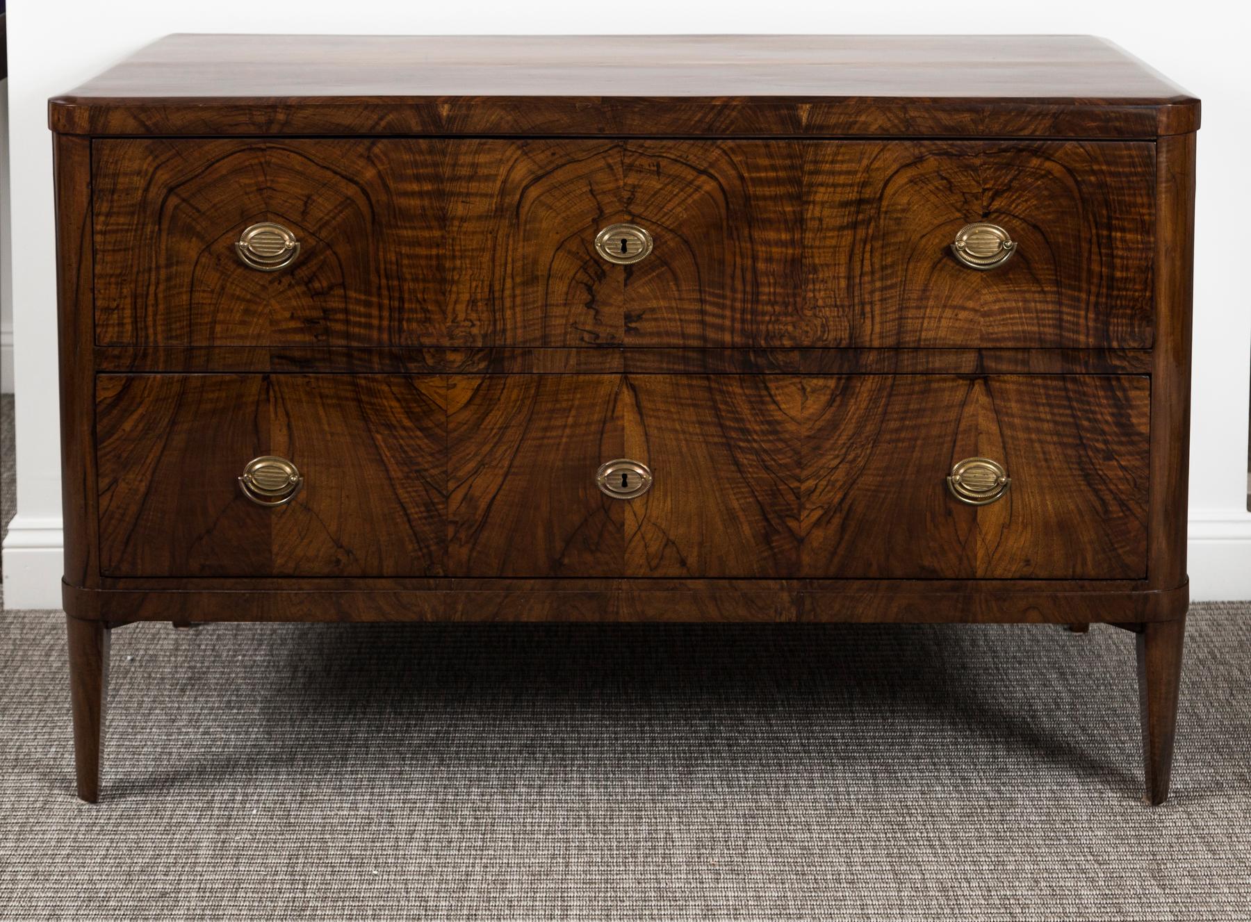 Extraordinary movement to this matchbook walnut veneer graces this finely composed two drawer chest shown with chamfered edges, finishing on tapered straight legs and embellished with original and finely chased bronze pulls.

Origin: Nussbaum,