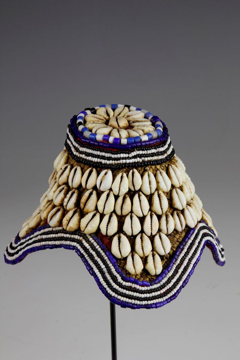 Traditionally worn as a symbol of rank and title, this beautiful Kuba chieftain's cap (laket mishiing) is embellished with cowrie shells and rows of blue, white and black glass beads. The body of the hat has been fashioned from raffia fibre using