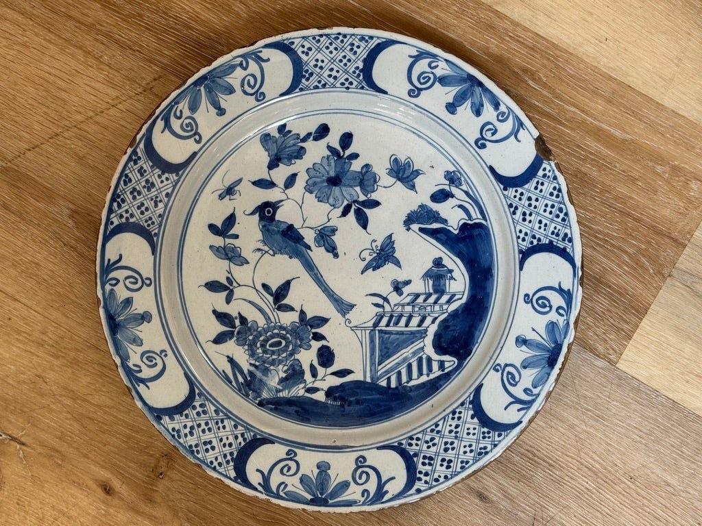 Ein feines englisches Delft-Geschirr mit einer Chinoiserie-Gartenszene mit Langschwanzvogel, Schmetterlingen und Bienen inmitten von Pfingstrosen und einem Zaun, gemalt in tiefem Kobaltblau auf einem zinnglasierten Grund. In der breiten Bordüre