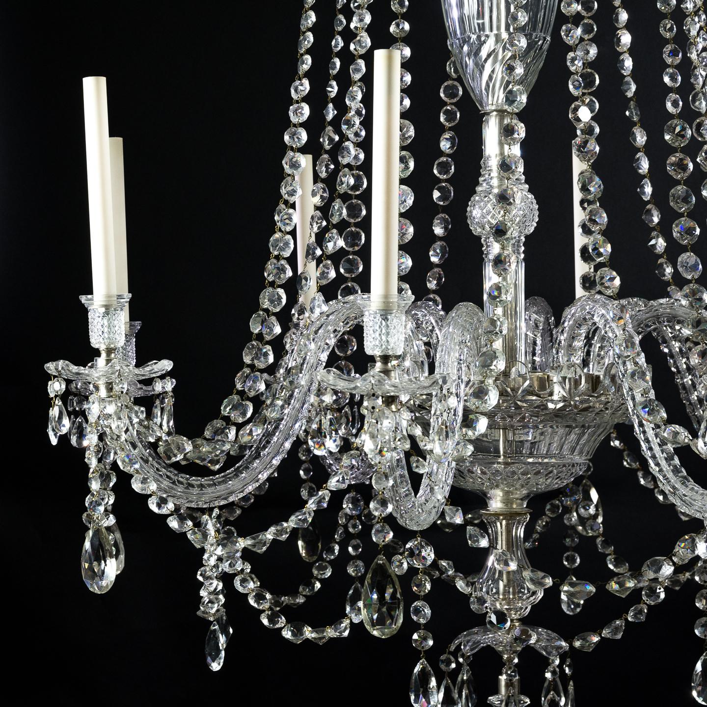 Un beau lustre en cristal de style géorgien anglais à huit lumières, début du 20ème siècle, dans la manière de F. & C. Osler Ltd, avec une couronne généreuse taillée en forme de queue d'aronde au-dessus d'une tige sectionnelle en forme de balustre,