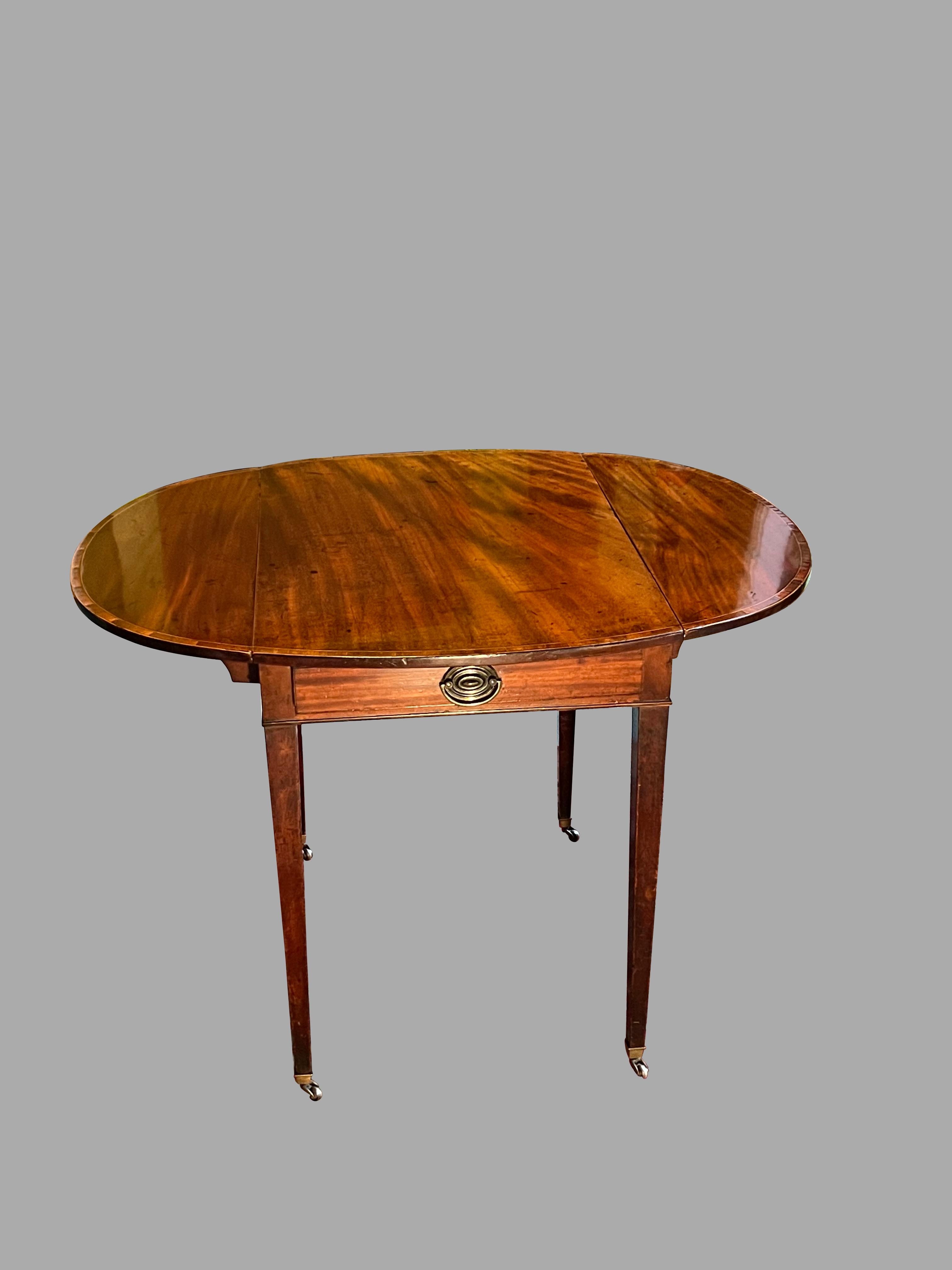 A fine English inlaid mahogany Hepplewhite period oval pembroke table of typical form, the crossbanded top with 2 drop sides over a single drawer, supported on square tapered legs ending in brass caps and casters. 
Lovely old color. This is an