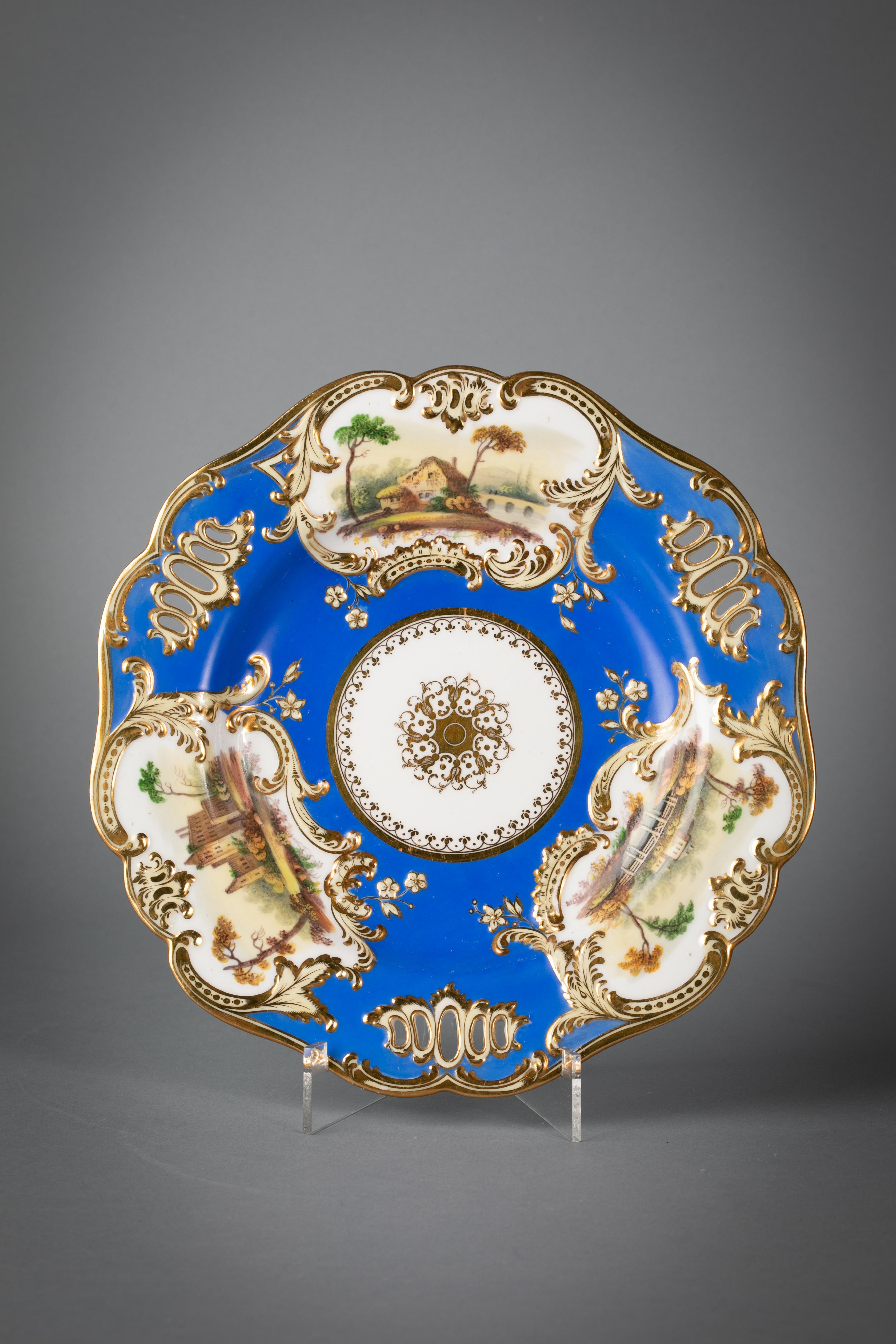 Comprising 24 plates, pair of covered sauce tureens and stands, pair of shell dishes and a pair of rectangular dishes. The bright blue ground interspersed with gilt-edged reticulation and with three rococo-formed cartouches edged in scrolls, molded
