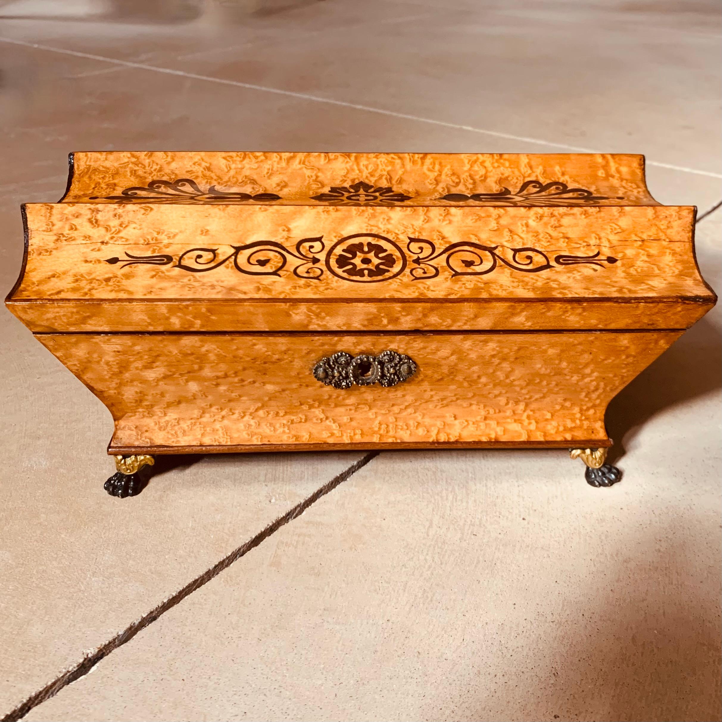 A very fine and exquisitely grained bird’s eye maple box of unusual form: the top curved into three concave channels, each one inlaid with contrasting anthemion and rosette designs. The interior is lined in cream silk with blue marbleized paper