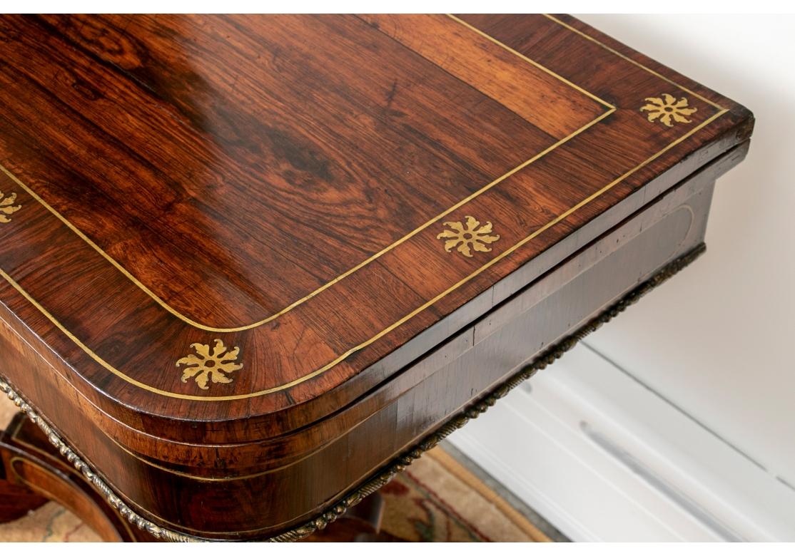 Very fine craftsmanship and inlays. The banded flip top with rounded corners with inlaid star motifs and brass string inlays. The apron with brass string inlays and a center panel with brass foliate scrolled motif. The top also swivels to reveal an