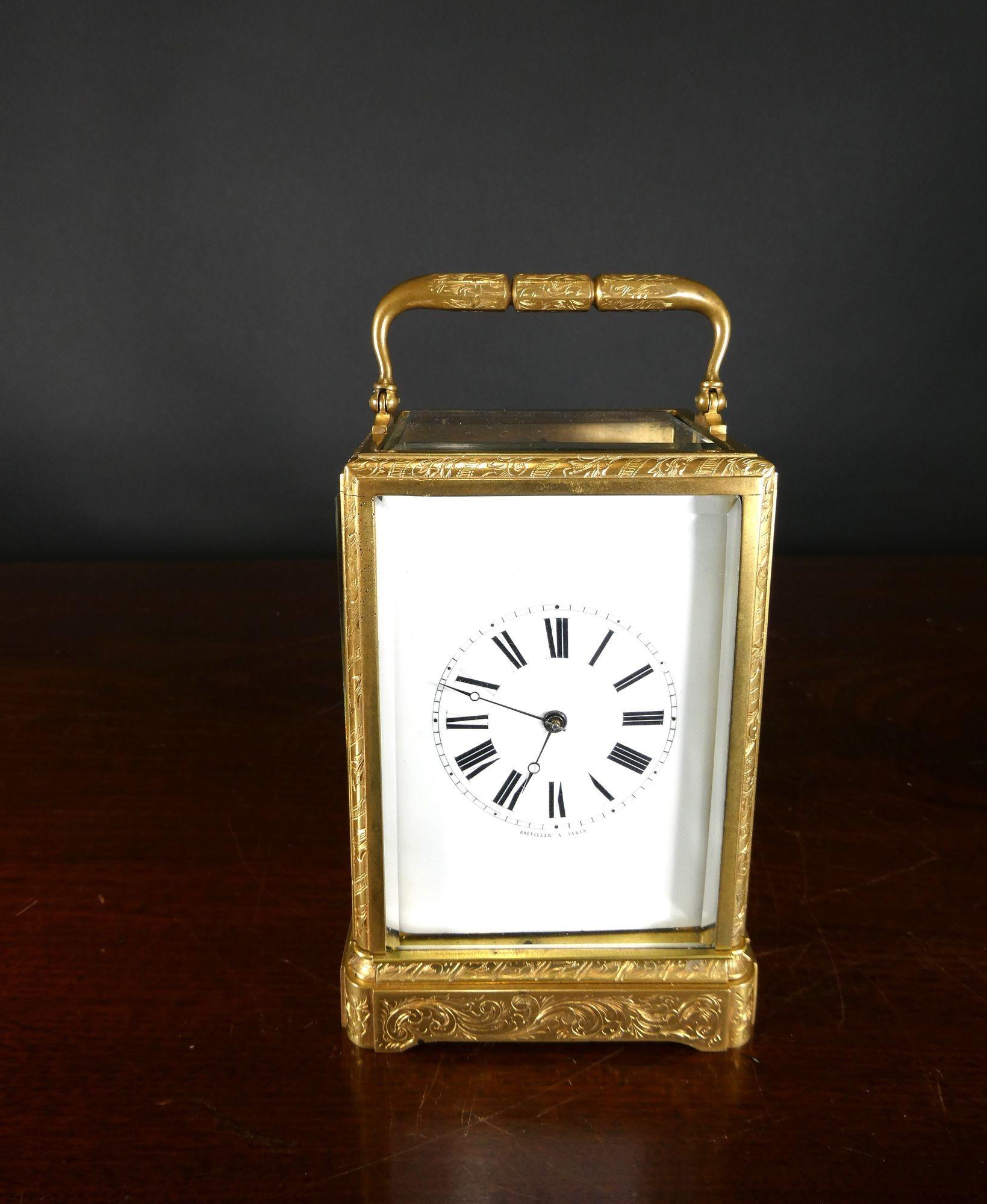 French gilded brass carriage clock in a finely engraved case with bevelled glass.

The rear of the case with conforming engraving to the rear door incorporating shutters for the winding and hand setting squares
Enamel dial with Roman numerals and