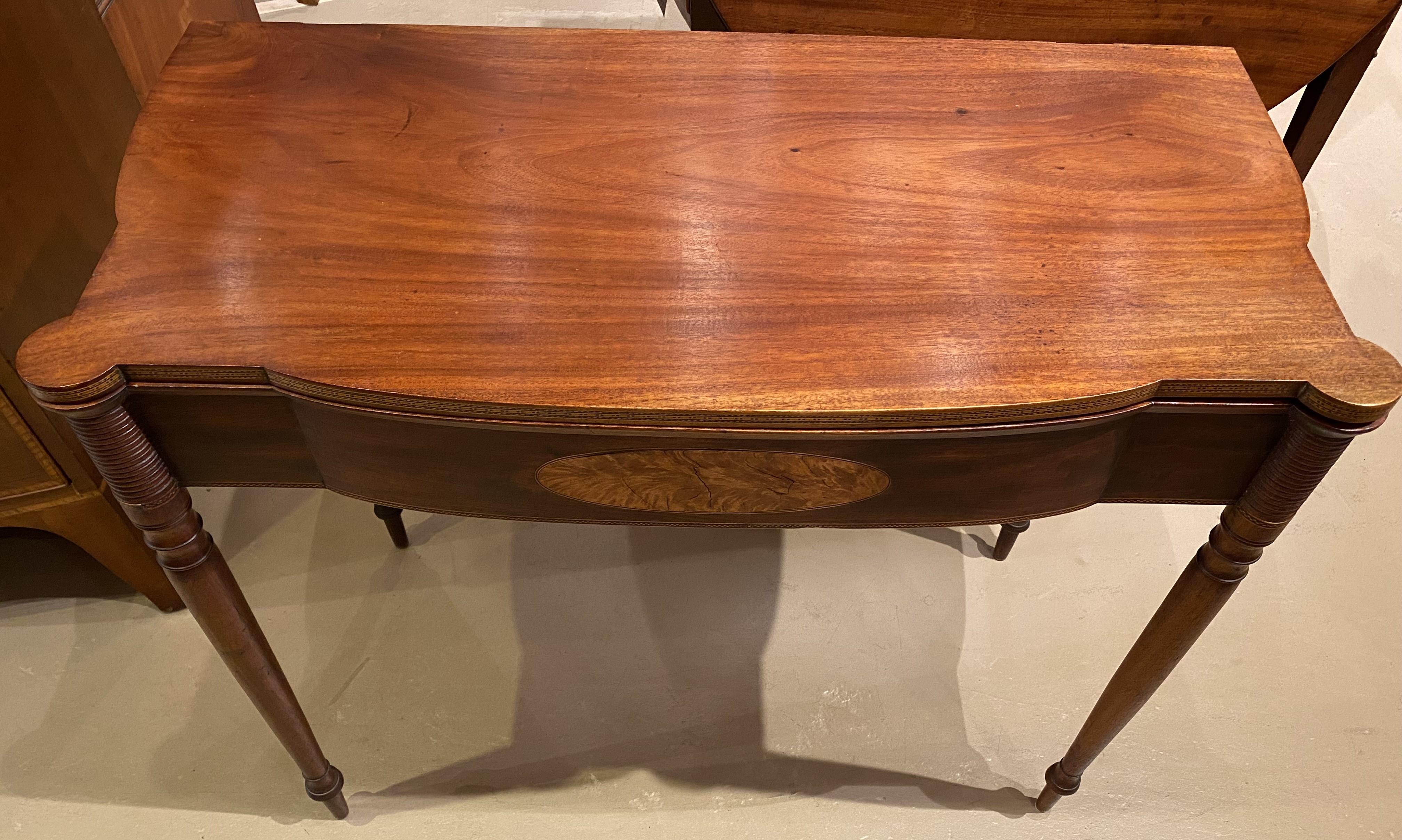 A fine example of a Federal Period, Sheraton mahogany card or gaming table with turret corners, checkered inlay around the folding top edge, a shaped frieze with an oval patera, all supported by nicely turned round tapered legs. Dates to circa